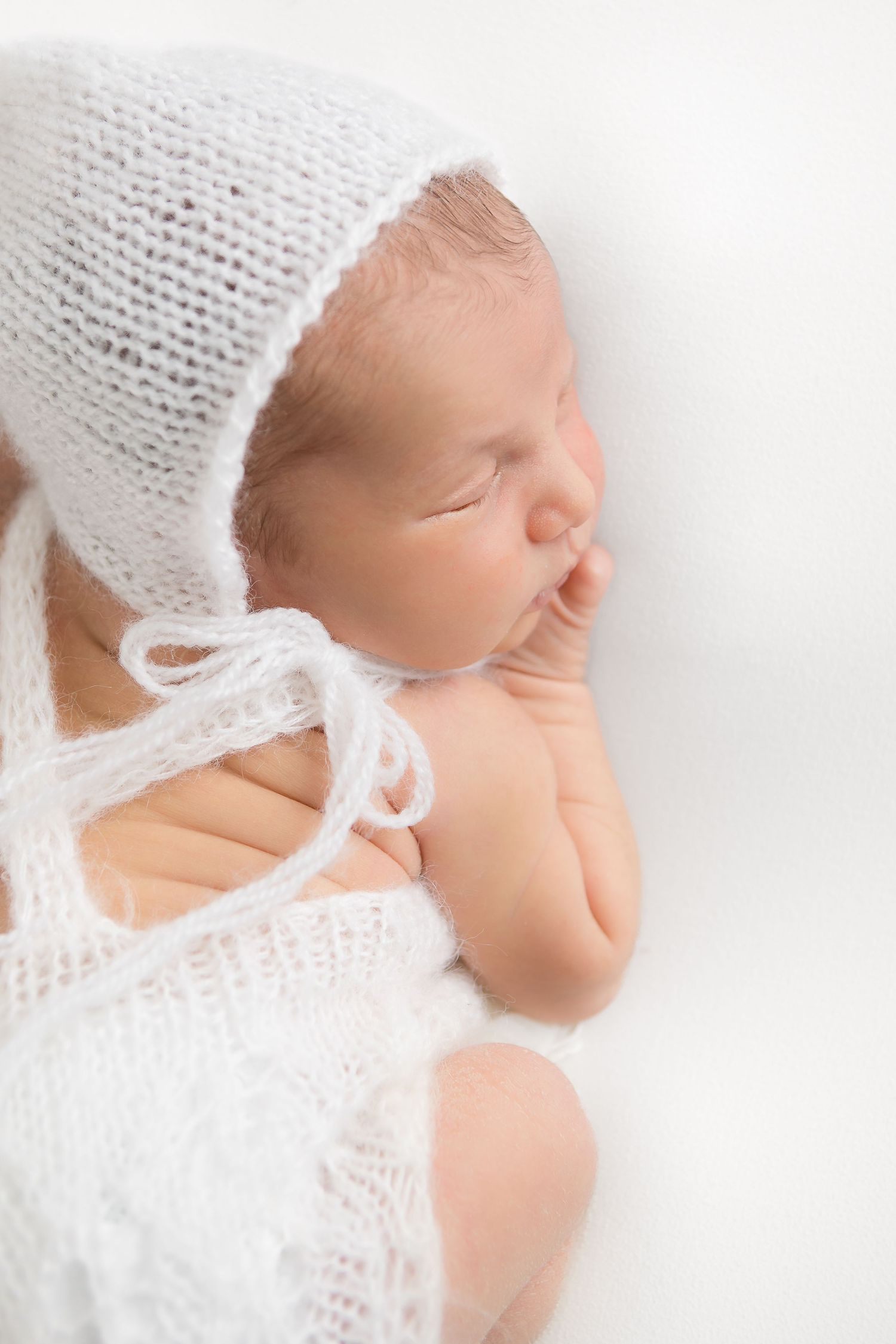 Serene portrait of sleeping baby wrapped in soft white knitted blanket.