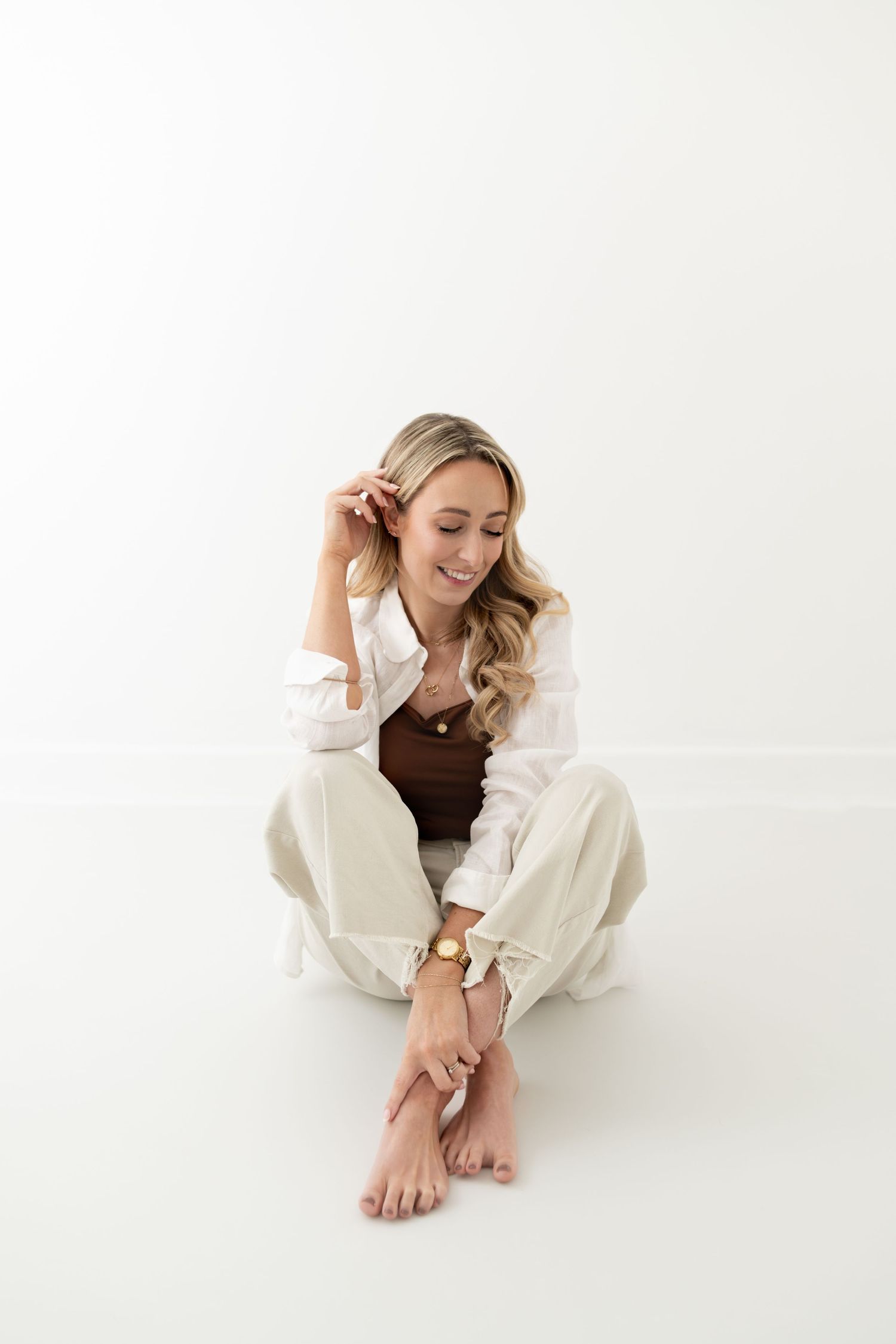Woman in cozy white sweater lounging in minimalist studio setting.