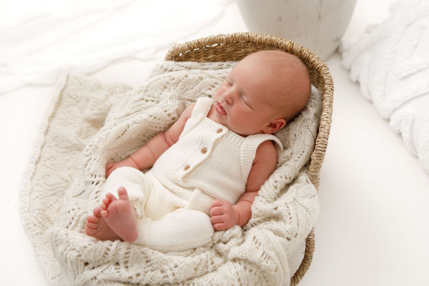 Newborn baby sleeping peacefully in white knitted wrap.