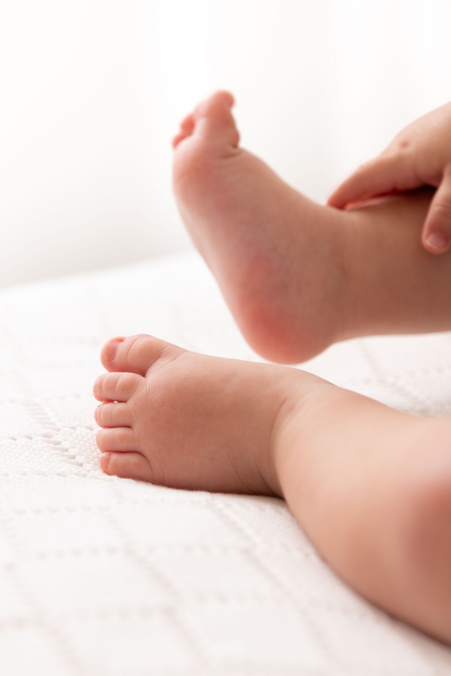 Close-up of tiny baby feet resting on a white textured blanket, with an adult hand gently holding one foot.