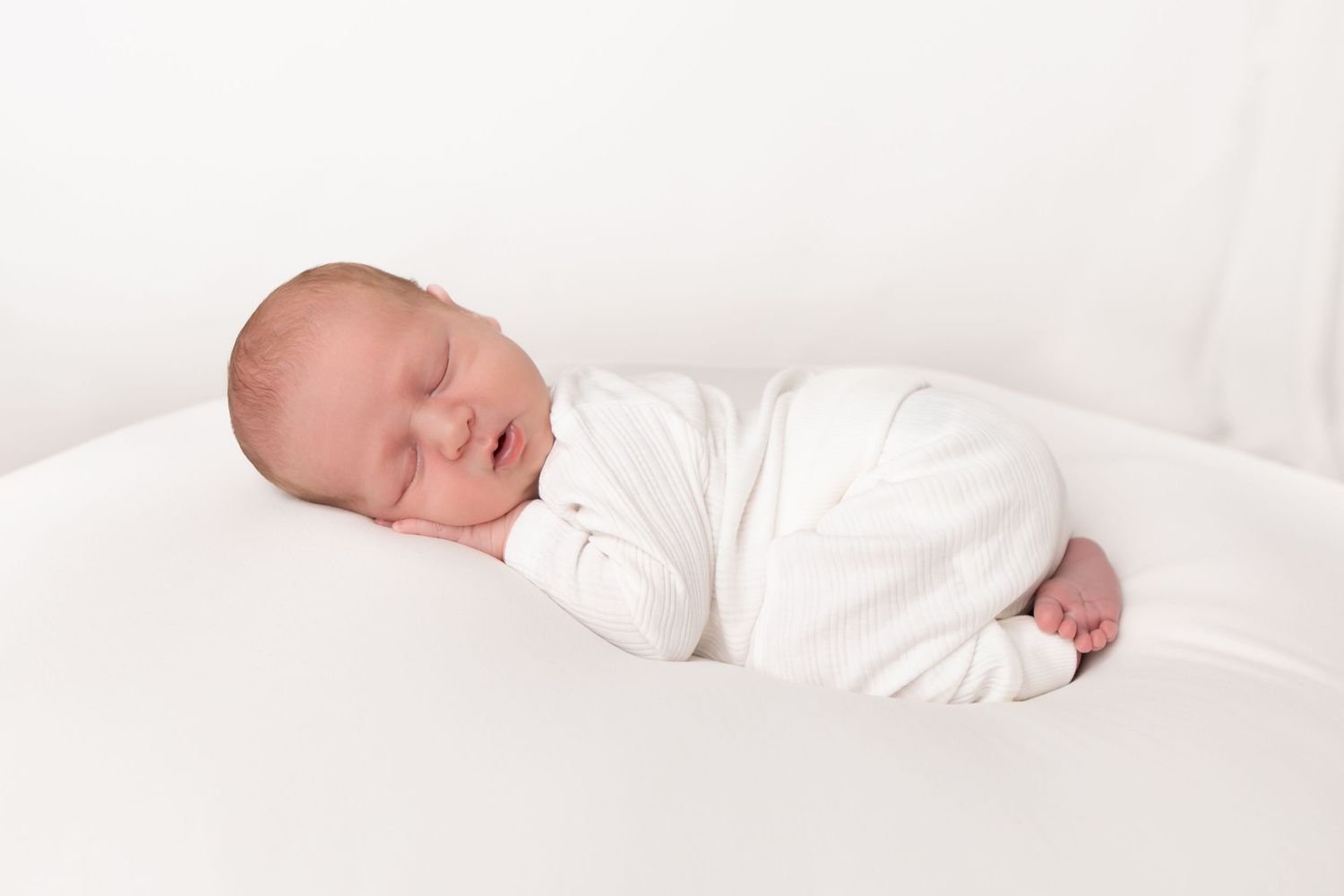 Peaceful newborn baby sleeping on white background, wrapped in white swaddle blanket.