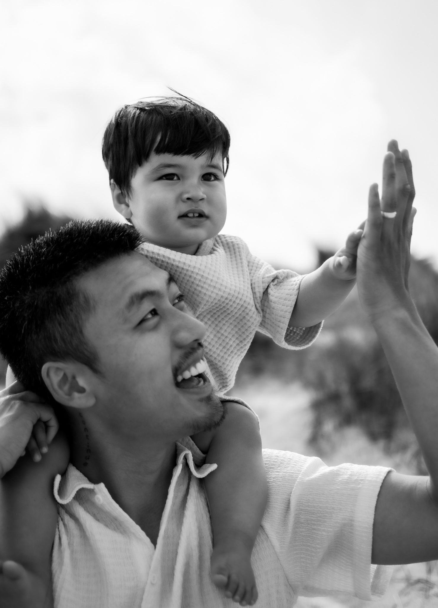 Black and white photo of a smiling man carrying a toddler on his shoulders, with the child reaching out.