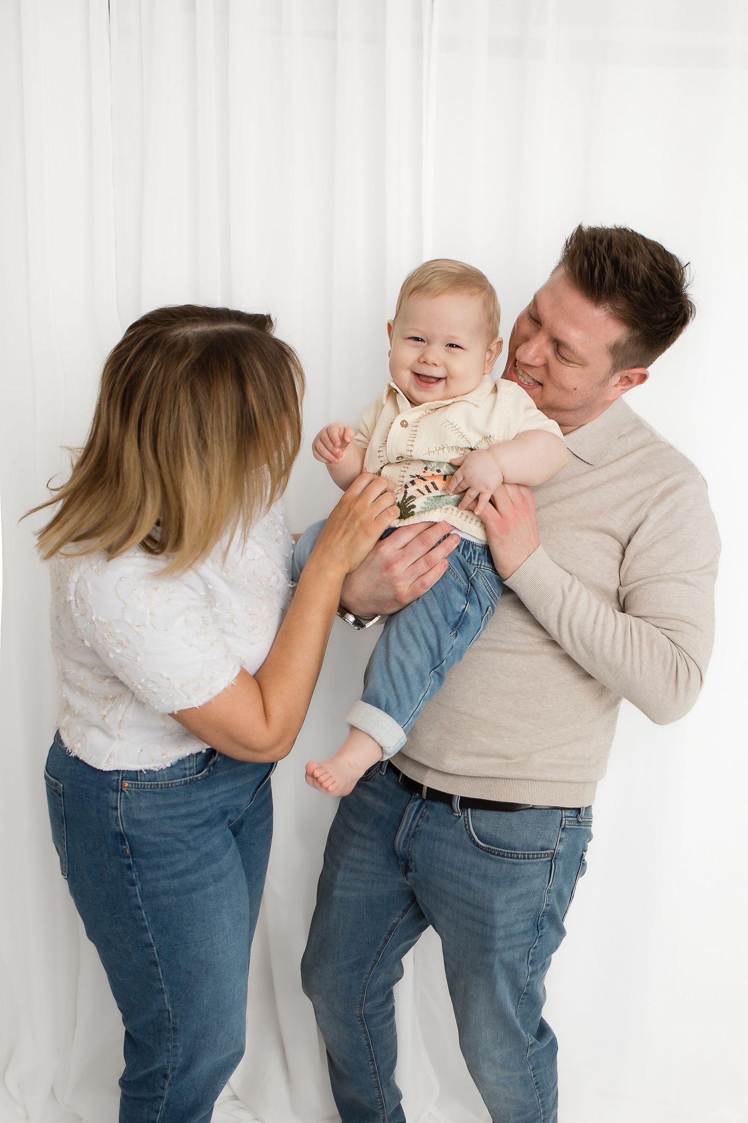 Playful studio photoshoot showing casual family interaction in jeans and neutral colors.