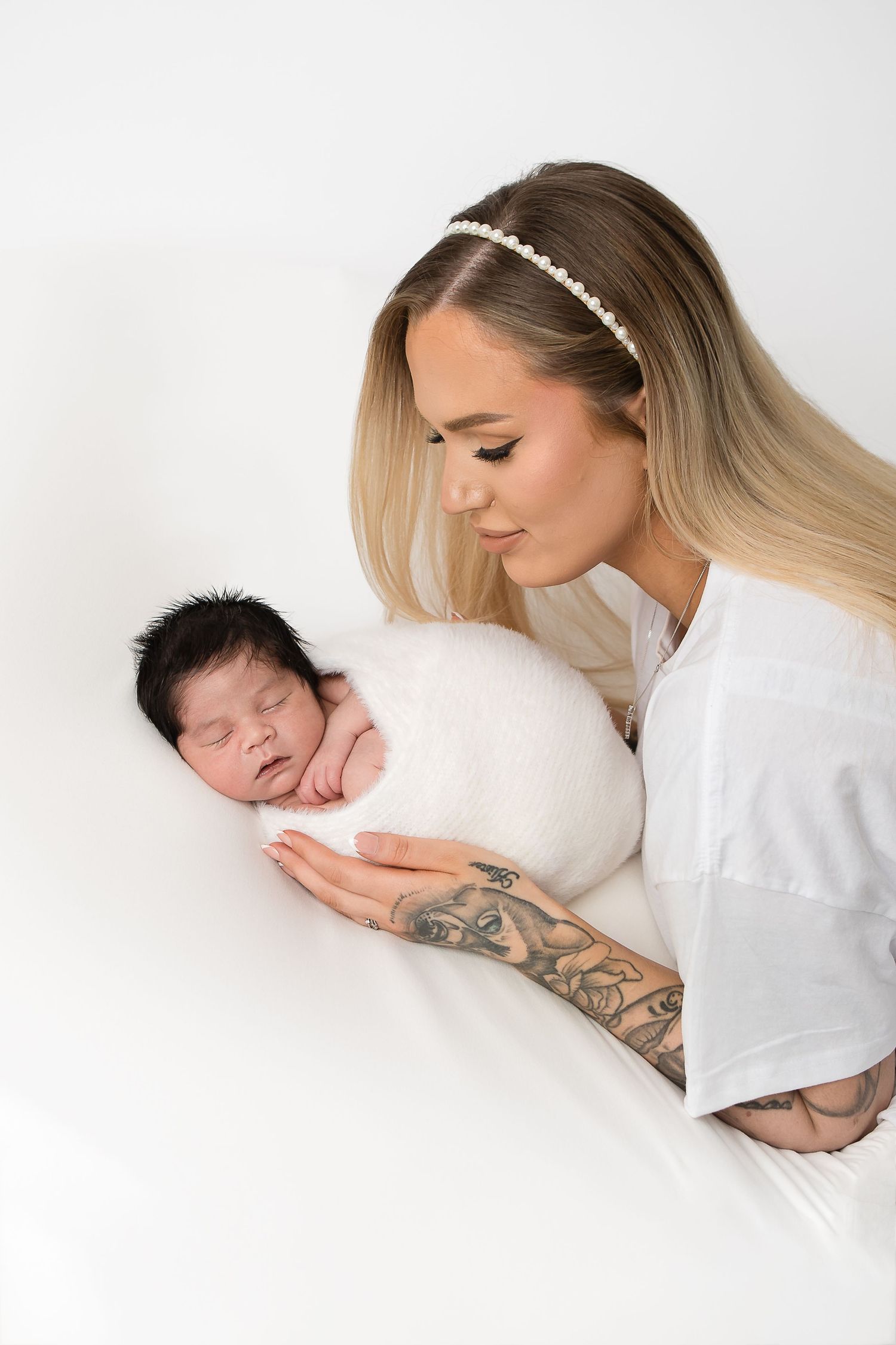 Tender moment between woman in white and sleeping newborn against white background.