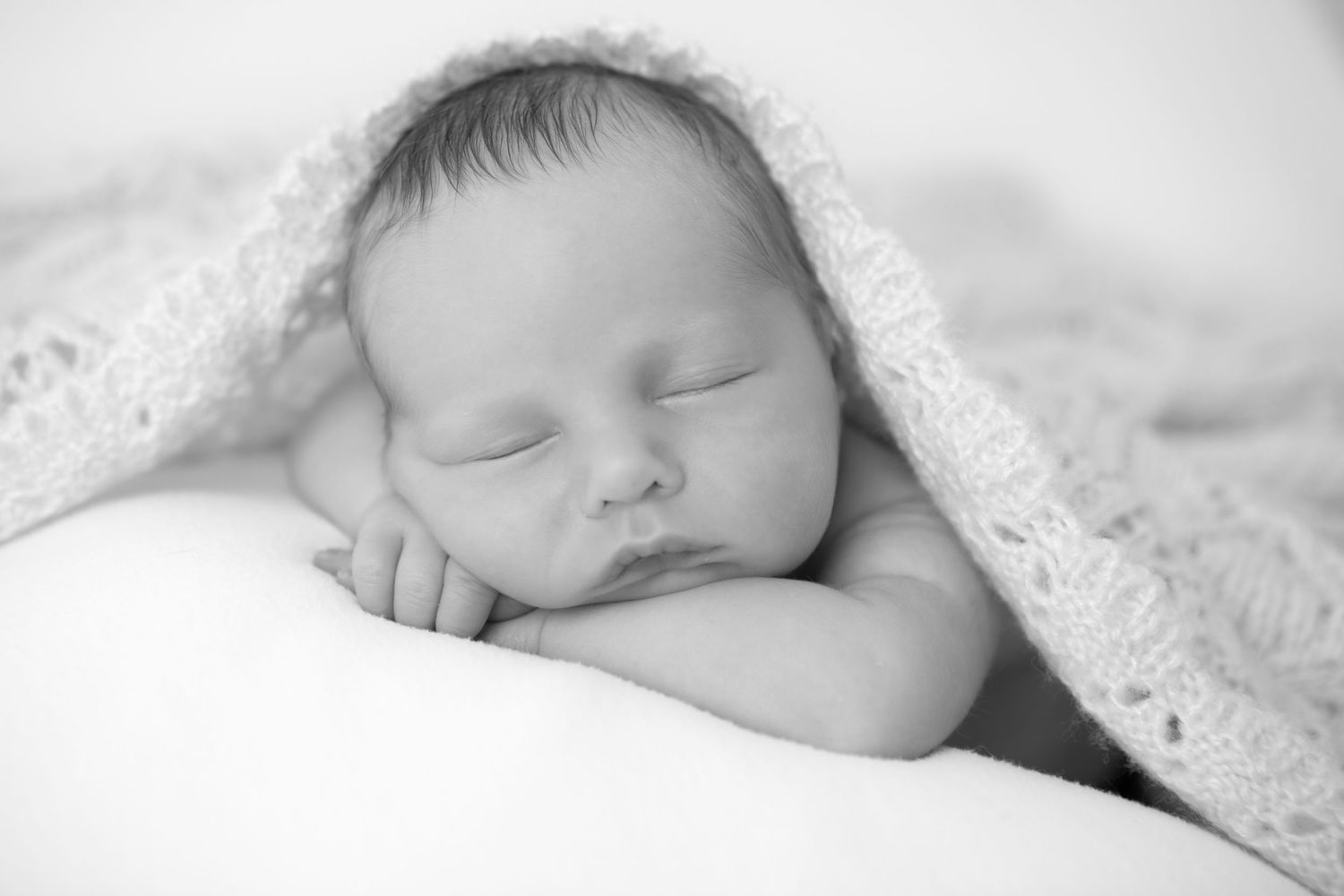 Black and white close-up of a sleeping newborn baby swaddled in soft white fabric.