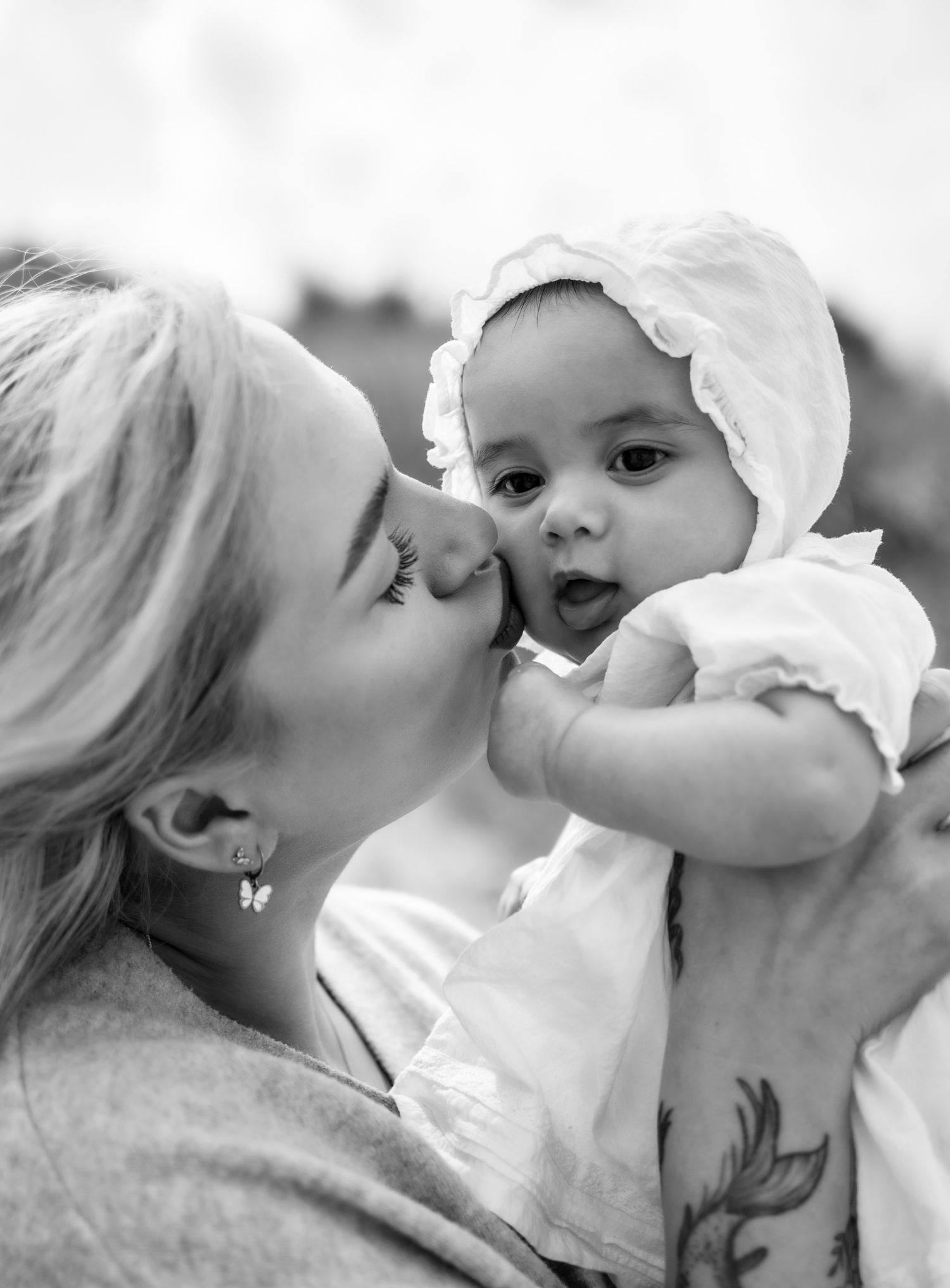 Black and white photo of a mother kissing her baby girl wearing a white bonnet.