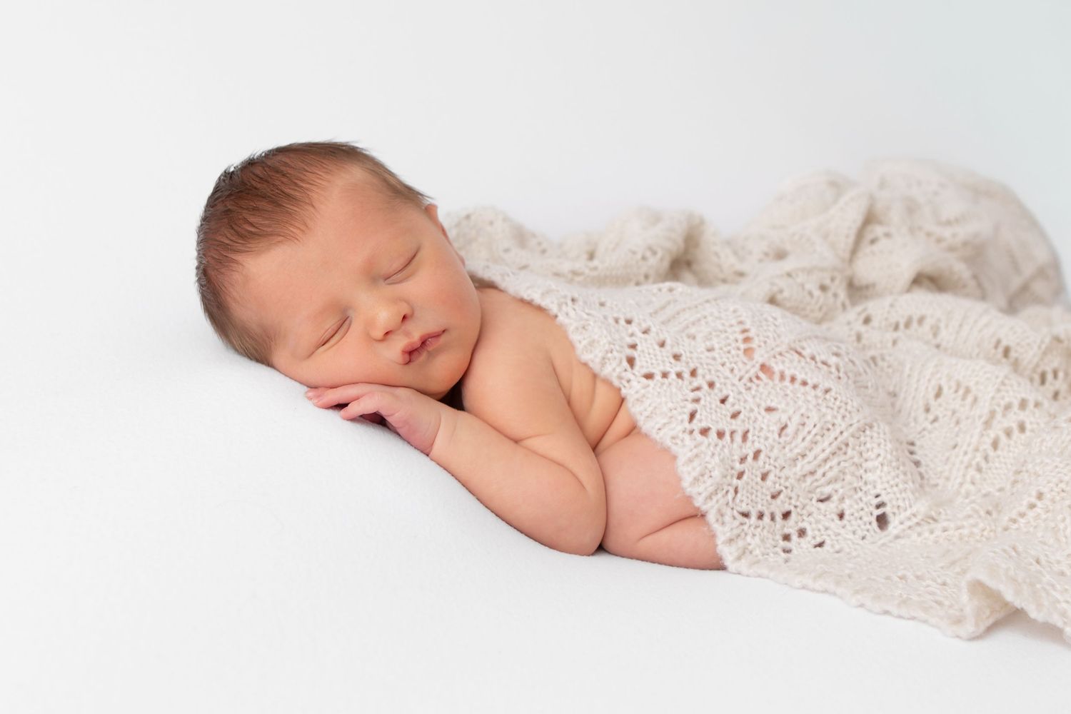 Peaceful newborn sleeping under delicate cream lace blanket.