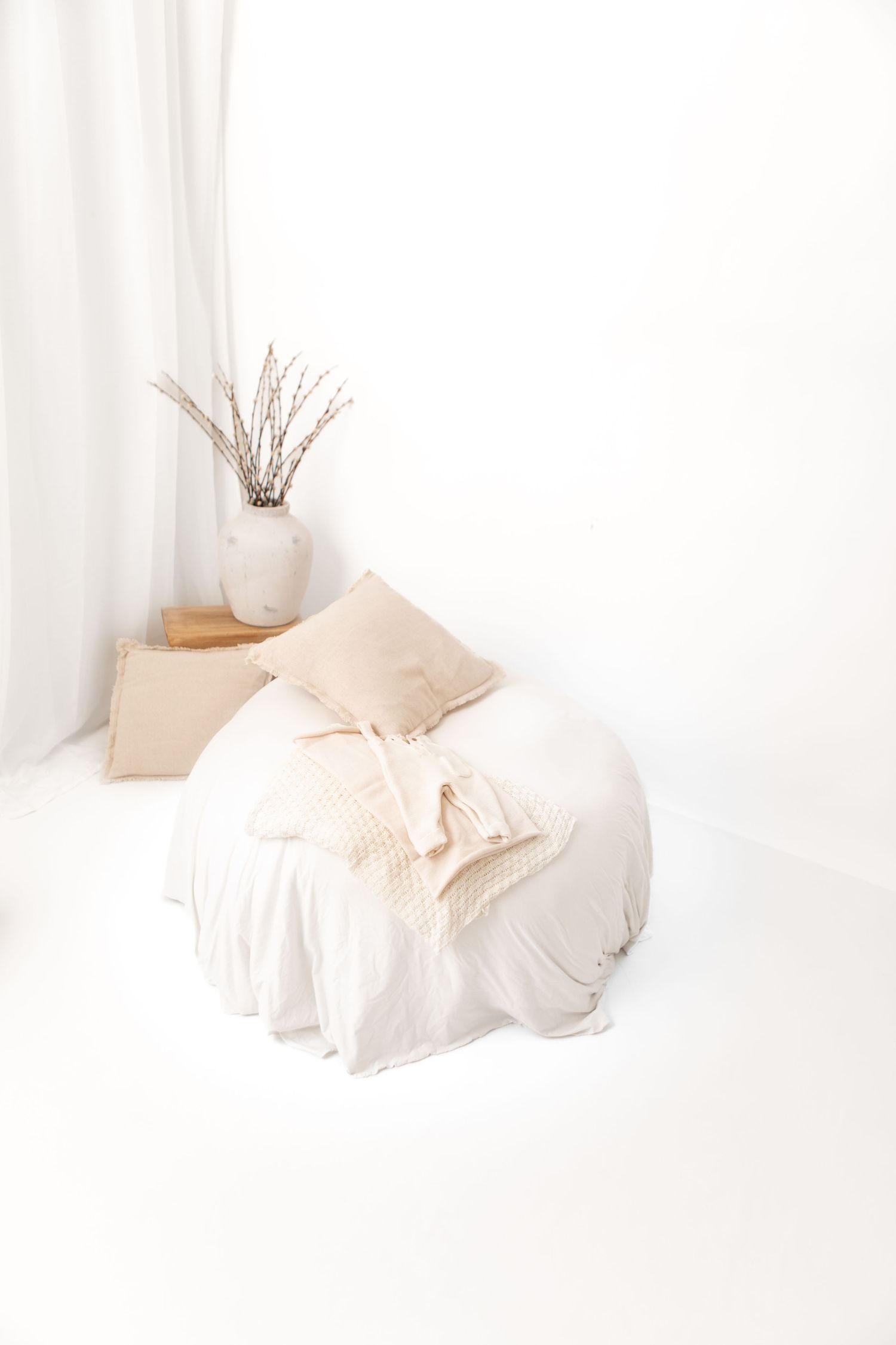 Minimalist bedroom interior with soft beige bedding and white curtains creating a serene, peaceful atmosphere.