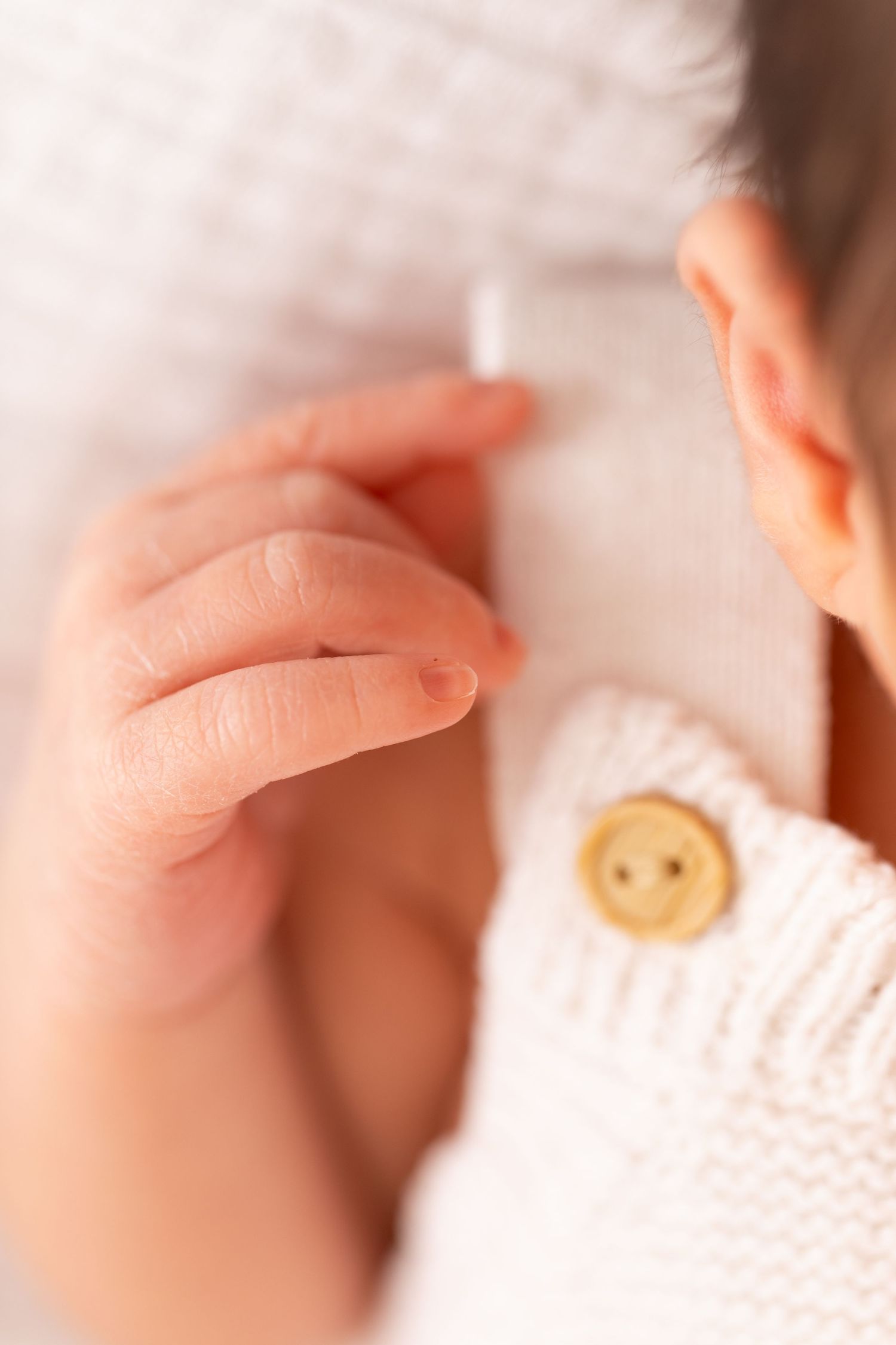 Close-up of a newborn baby's tiny hand resting on a white knit sweater with a wooden button.