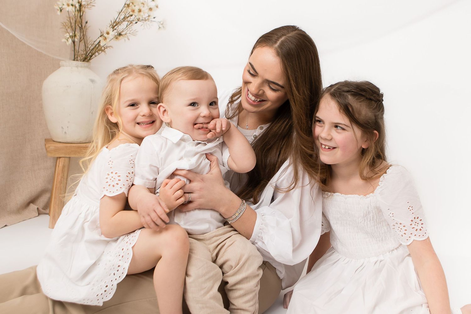 Family group seated together in white outfits sharing happy moment against neutral background.