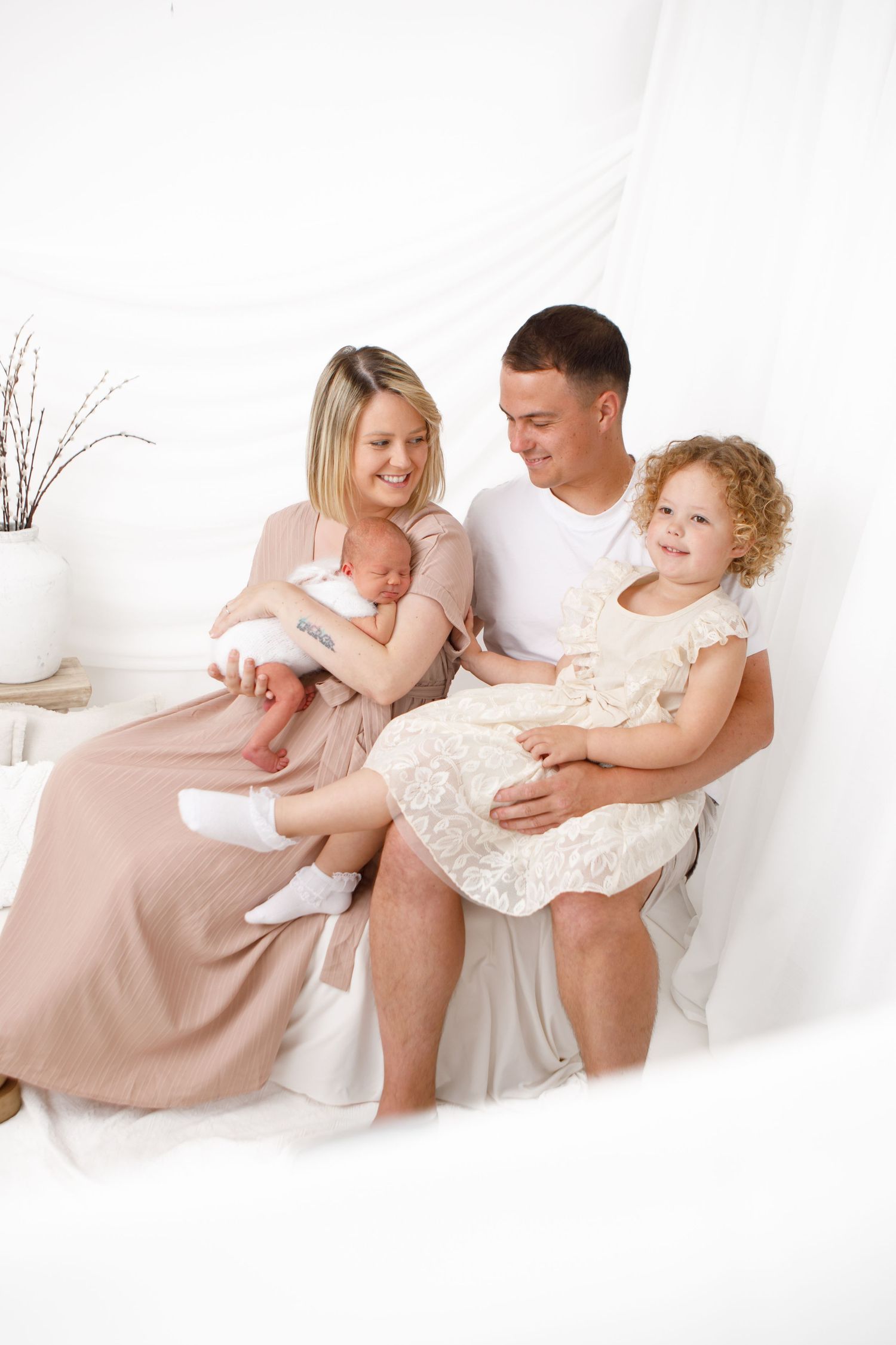 Family lounging together in white studio setting with soft natural lighting.