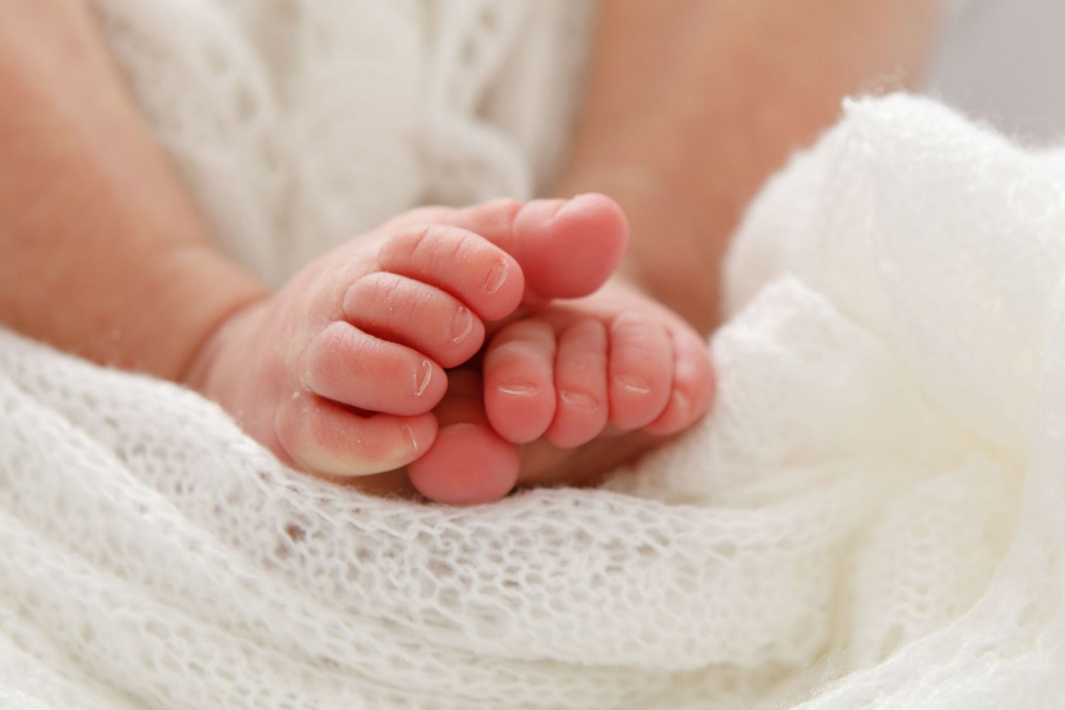 Tiny baby feet nestled in white lace fabric.