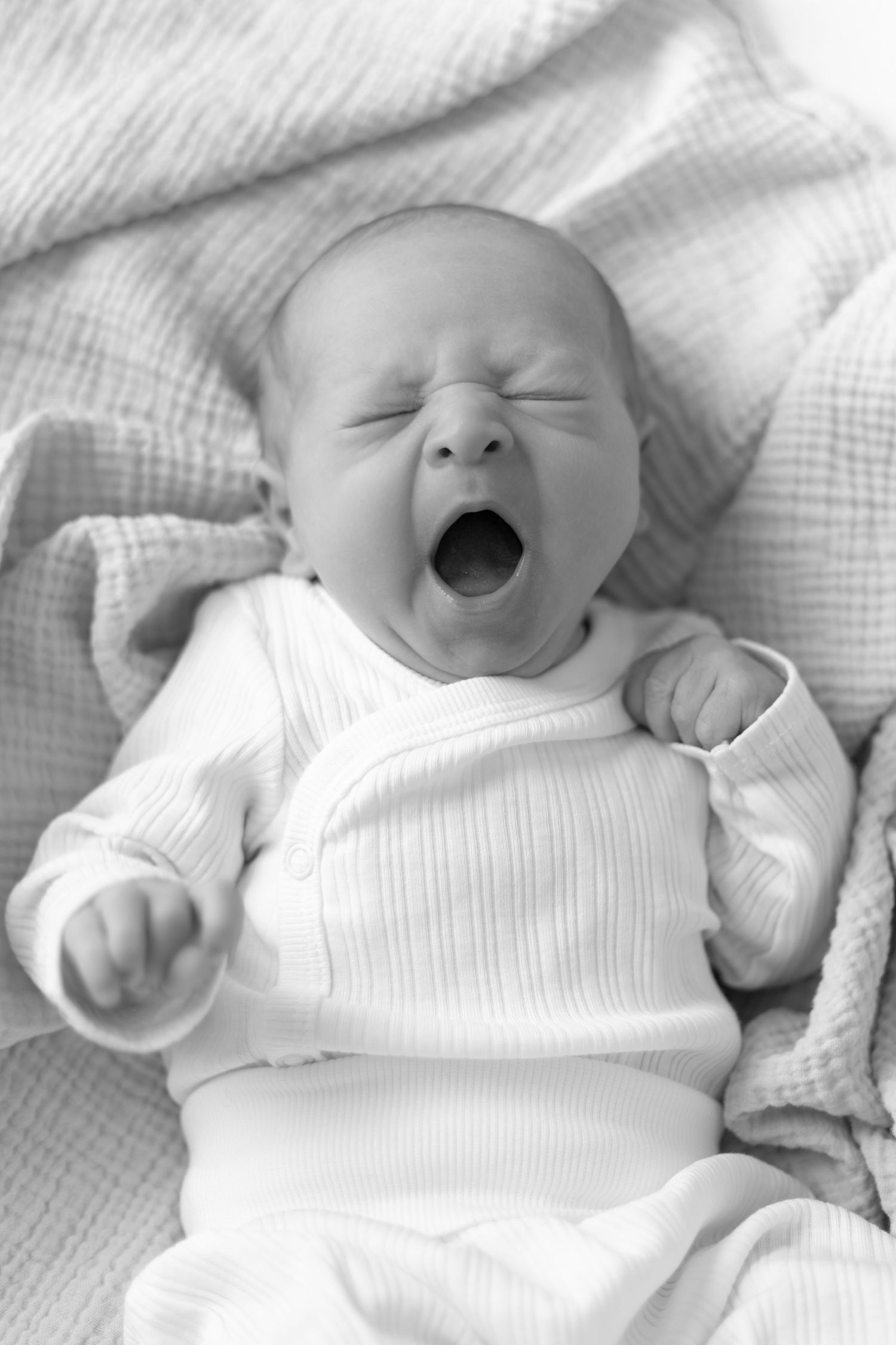 Series of black and white photos showing a baby in white clothing making expressive faces.