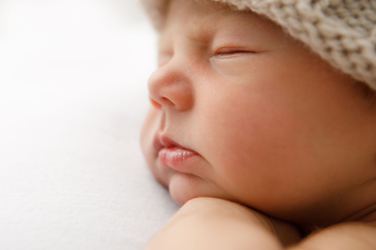 Sleeping newborn wearing knitted cream colored hat.
