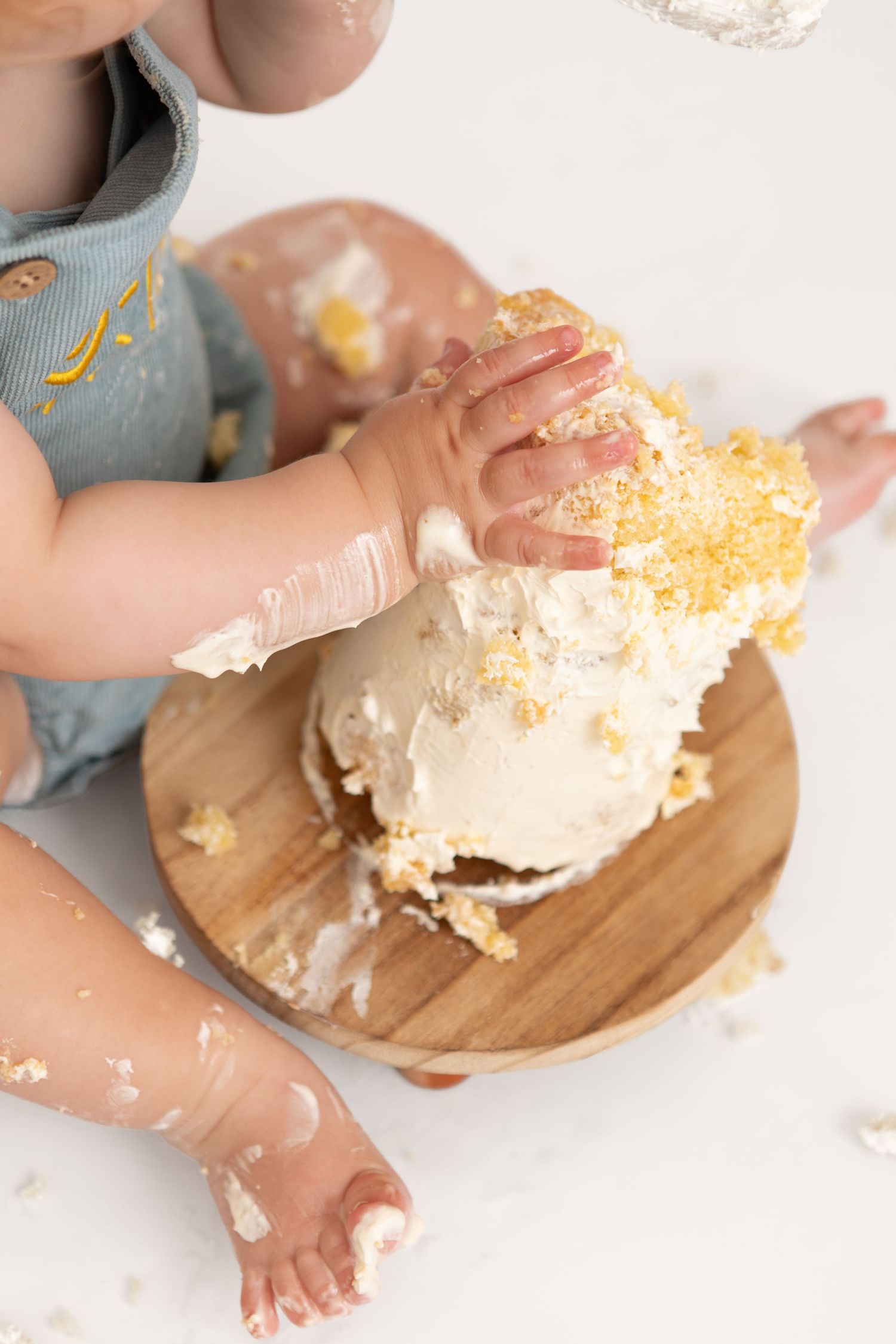 Baby smashing a white frosted cake on a wooden board during a first birthday cake smash photo session.