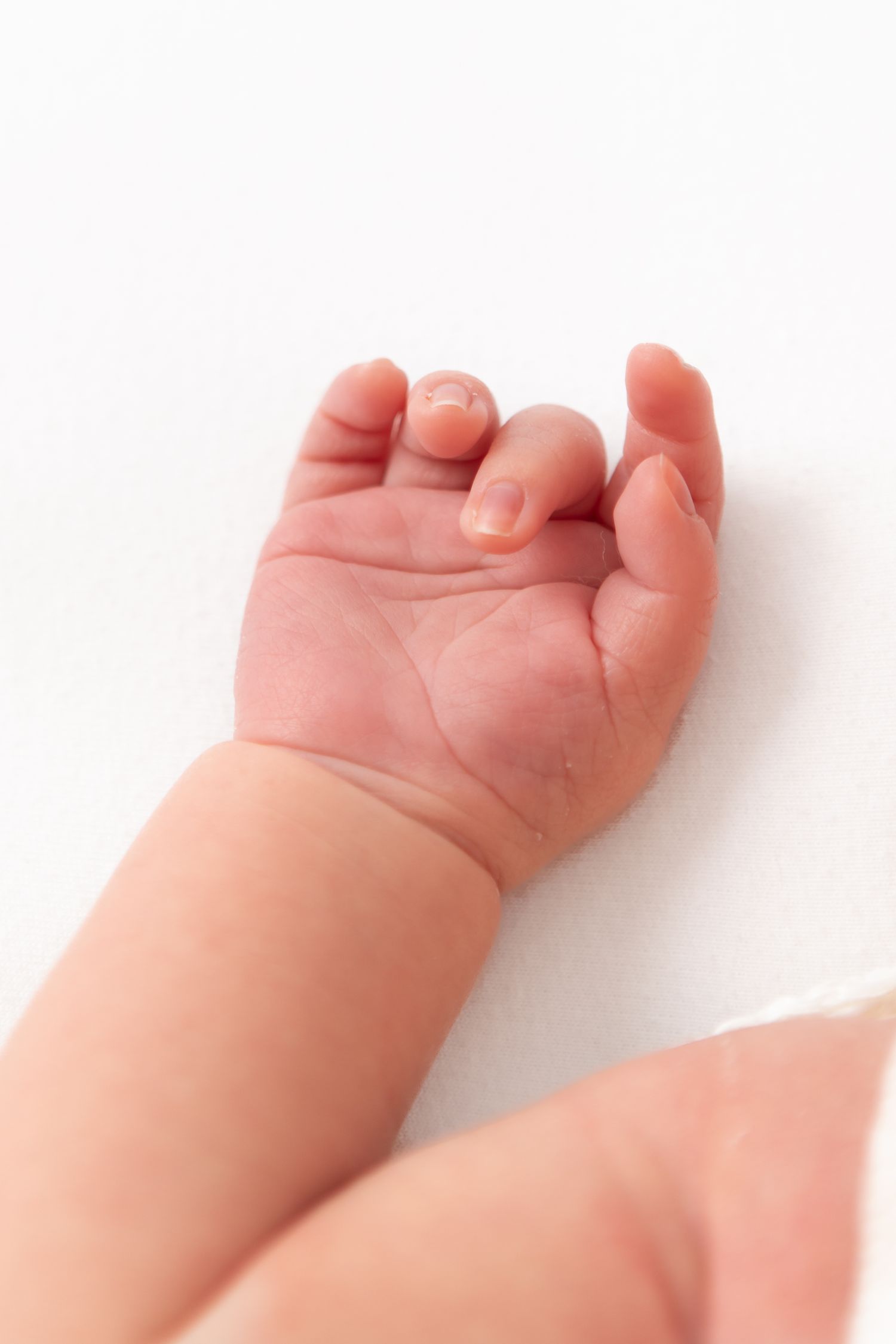 Close-up of a newborn baby's tiny open hand resting on a white surface, showing delicate fingers and soft skin.
