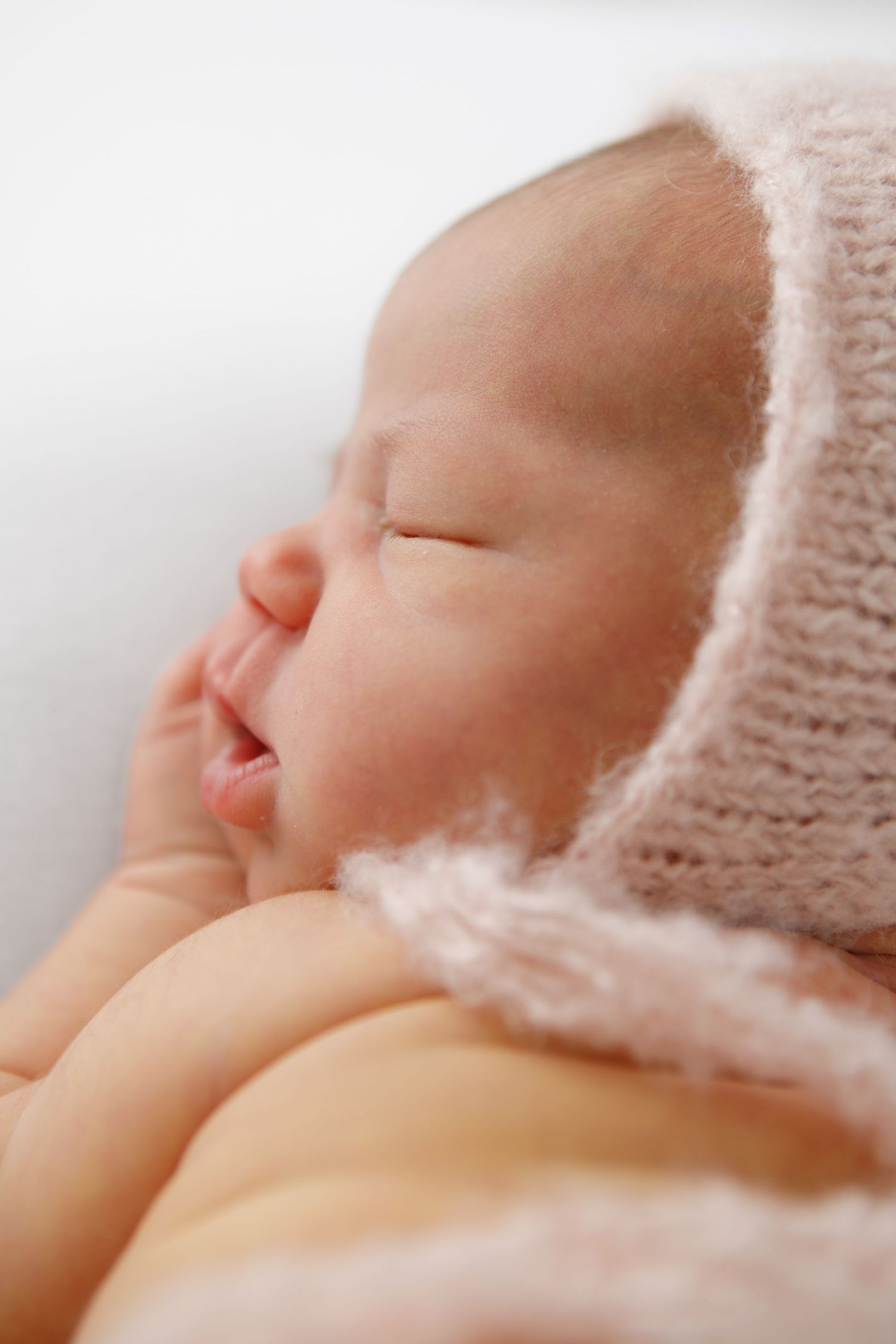 Serene close-up portrait of sleeping newborn wearing knit bonnet in warm tones.