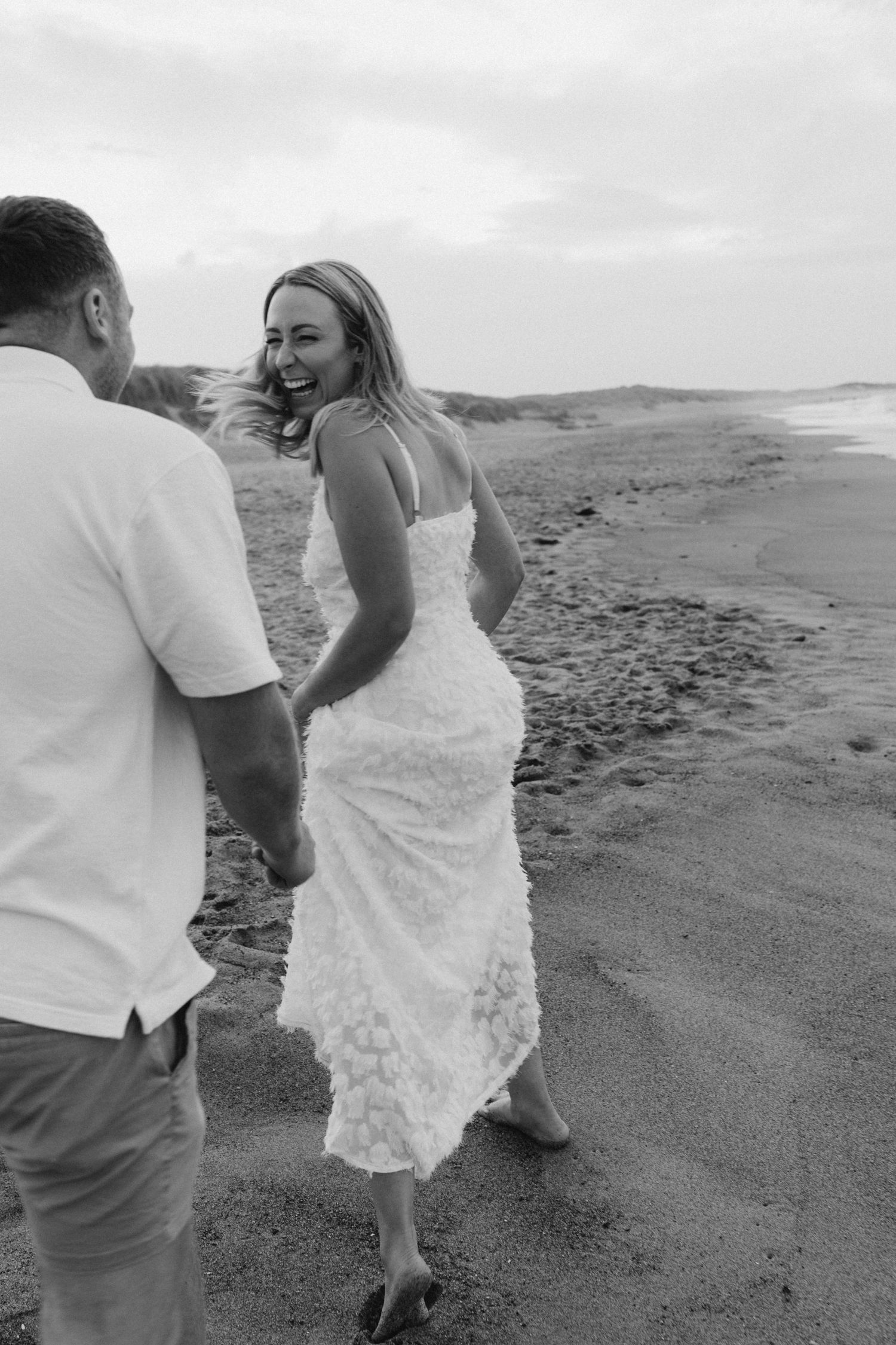 A couple walks along a scenic beach shoreline in black and white.