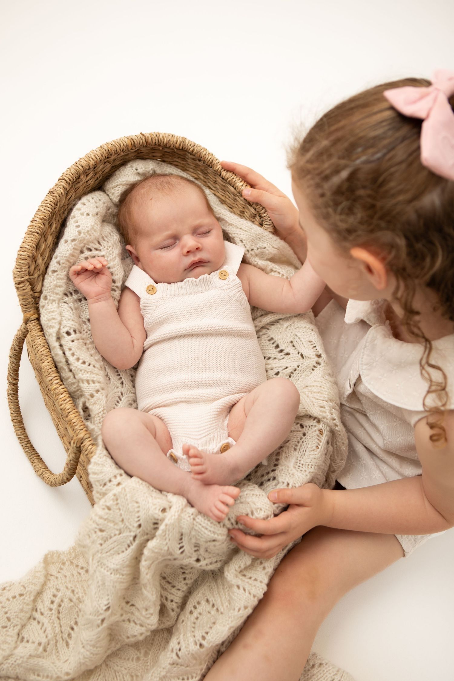 Baby sleeping peacefully in woven basket with sibling looking on.
