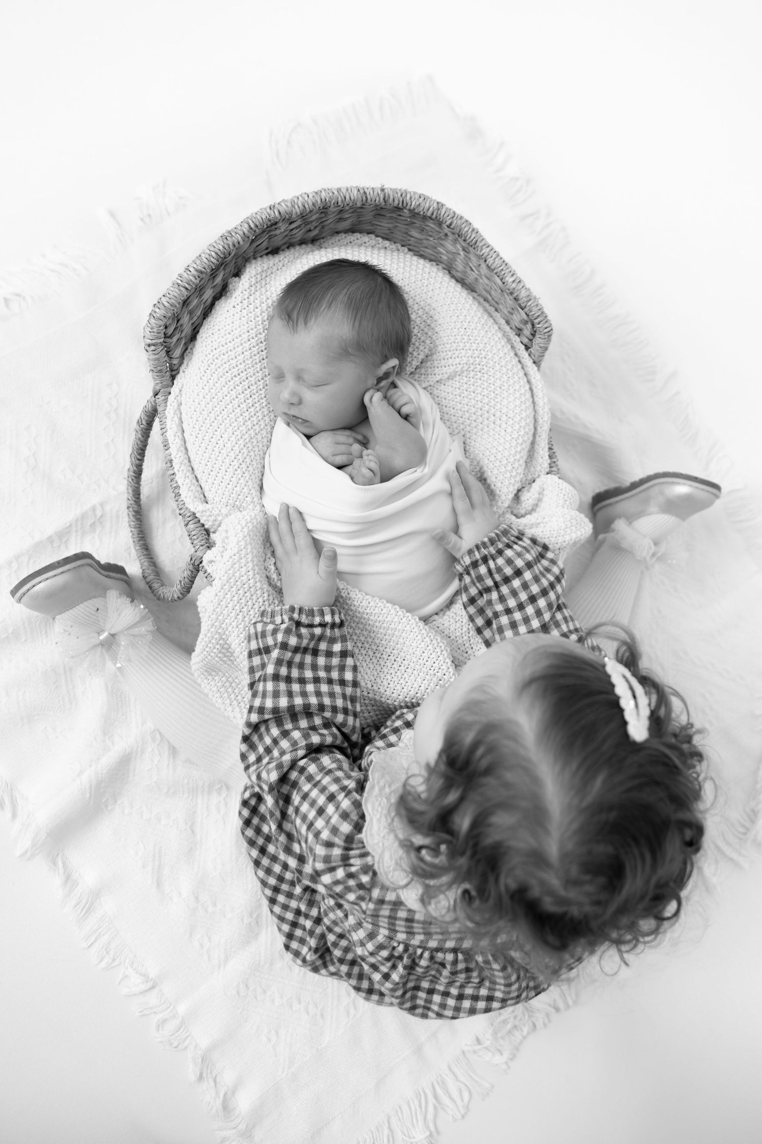 Overhead view of a baby and toddler in matching checkered outfits lying on white blanket.