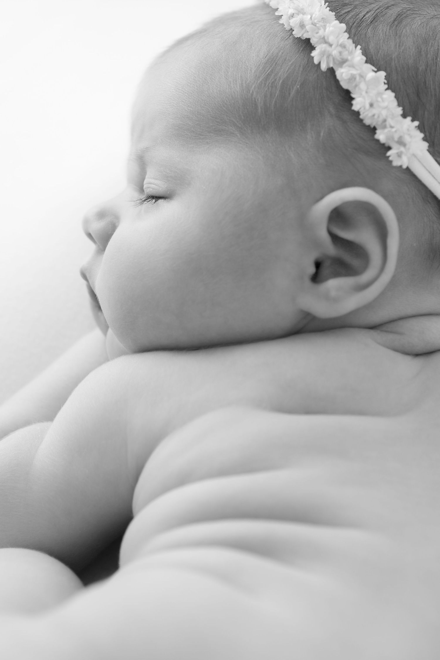 Delicate close-up of sleeping baby wearing lace headband in soft black and white.