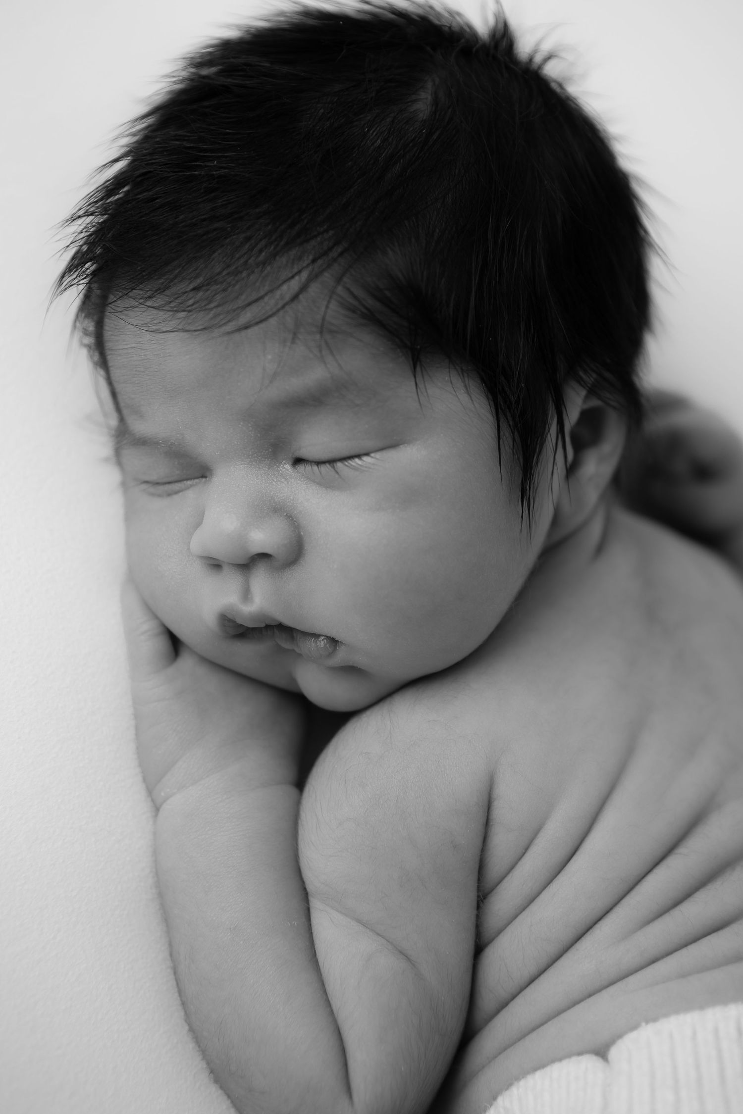 Peaceful sleeping newborn with dark hair photographed in black and white.