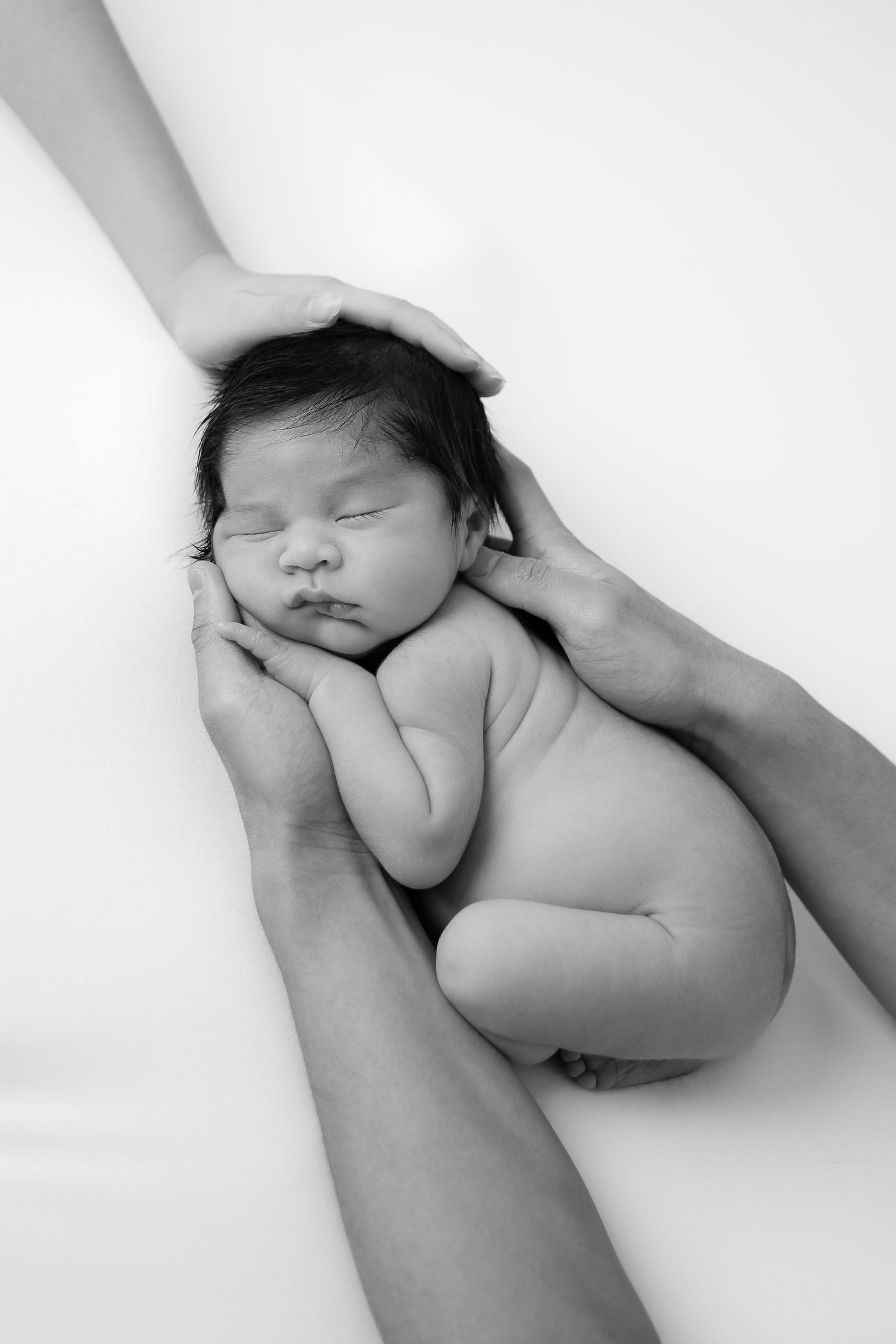 Minimalist black and white photo of hands cradling sleeping newborn.
