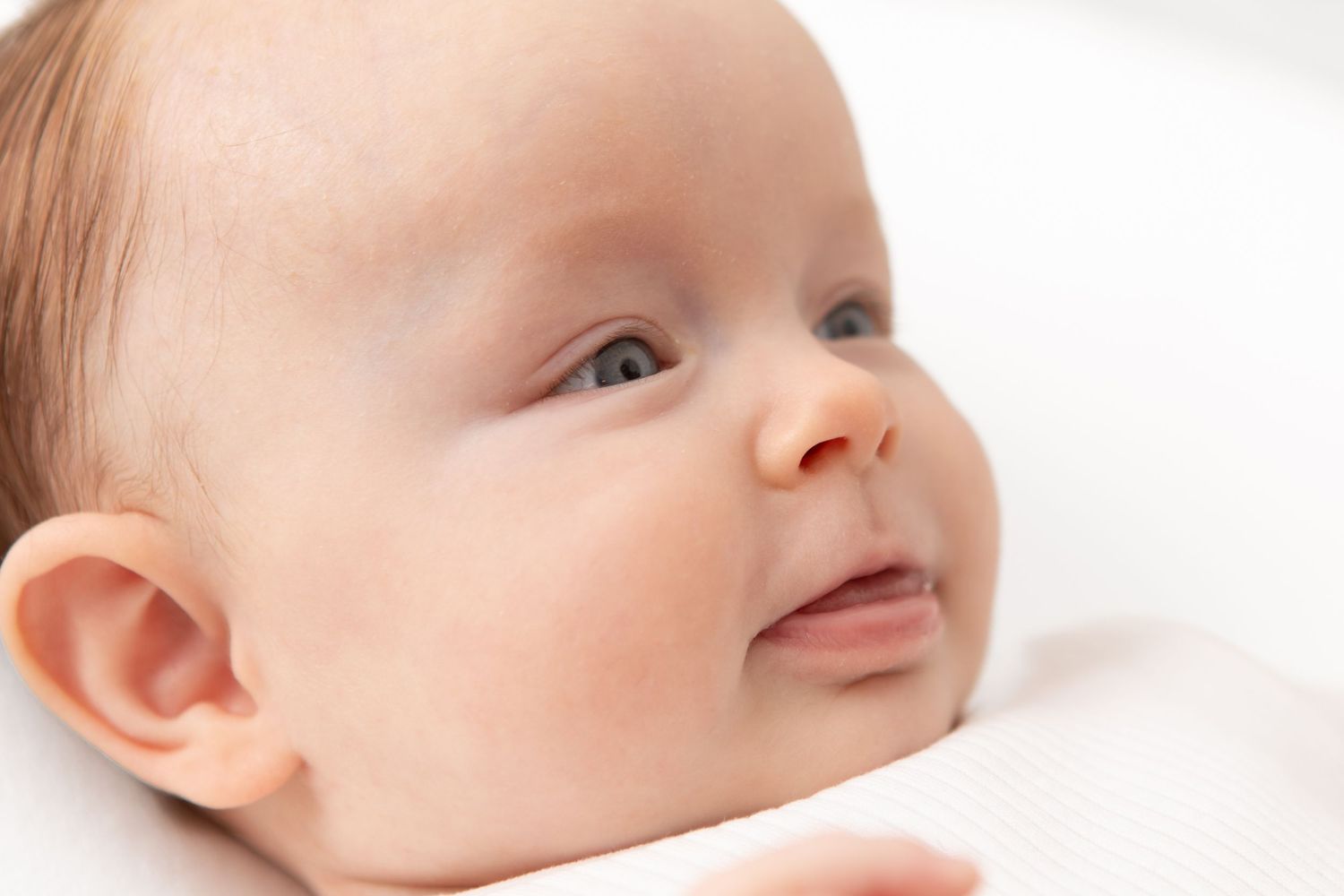 Close-up portrait of a peaceful newborn baby with blue eyes lying on a white background.