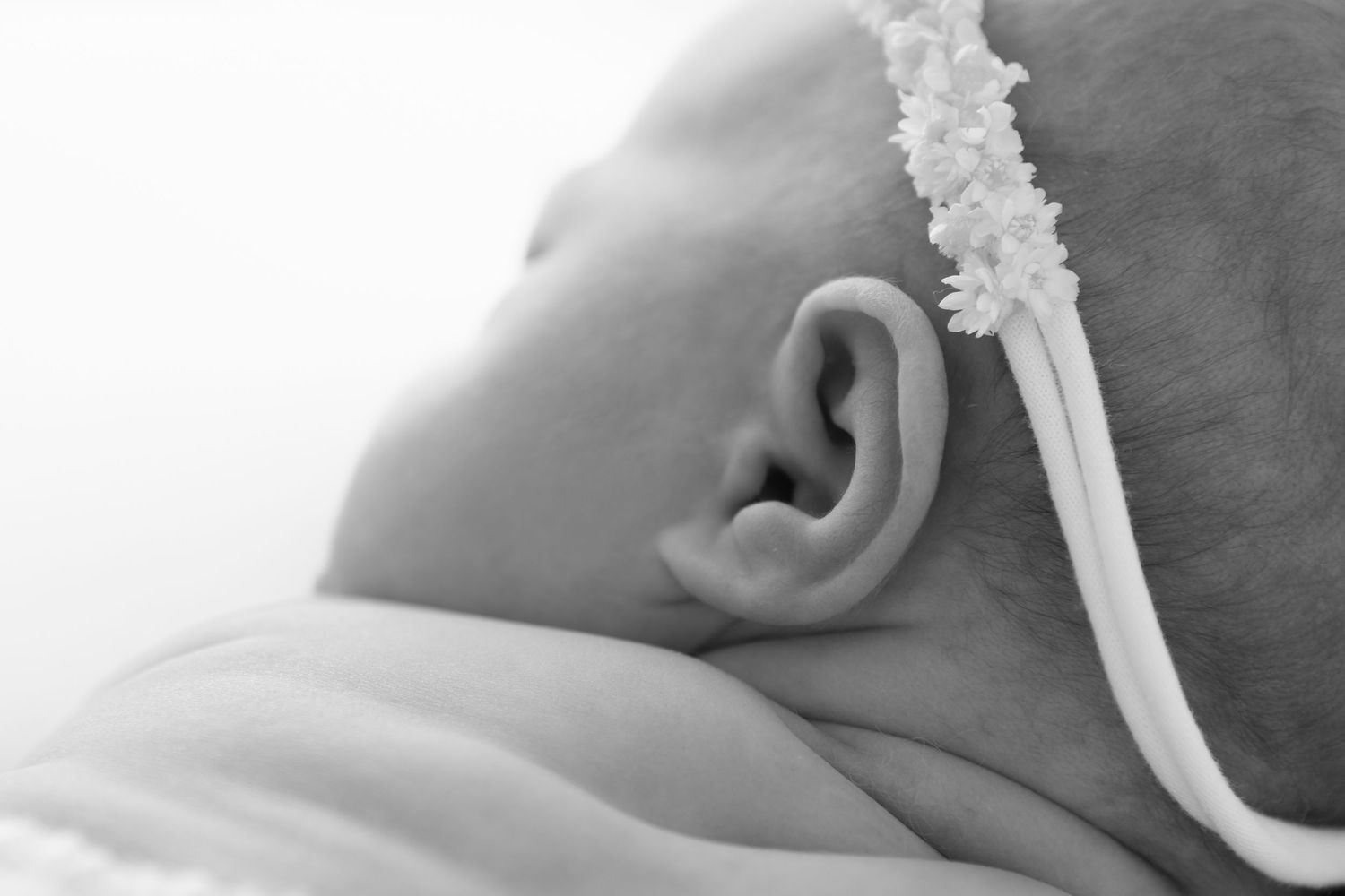 Black and white close-up of a newborn baby's ear and feeding tube against a soft background.