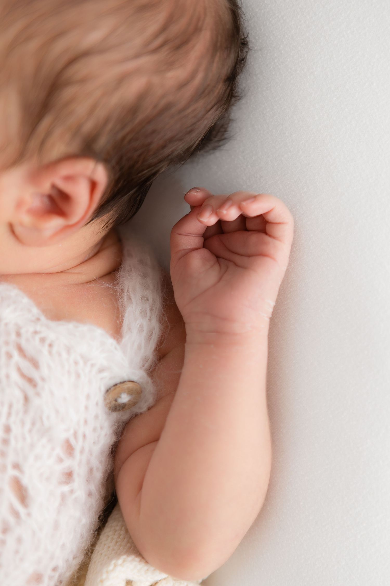 Sleeping newborn wearing lace with tiny hand curled near face.