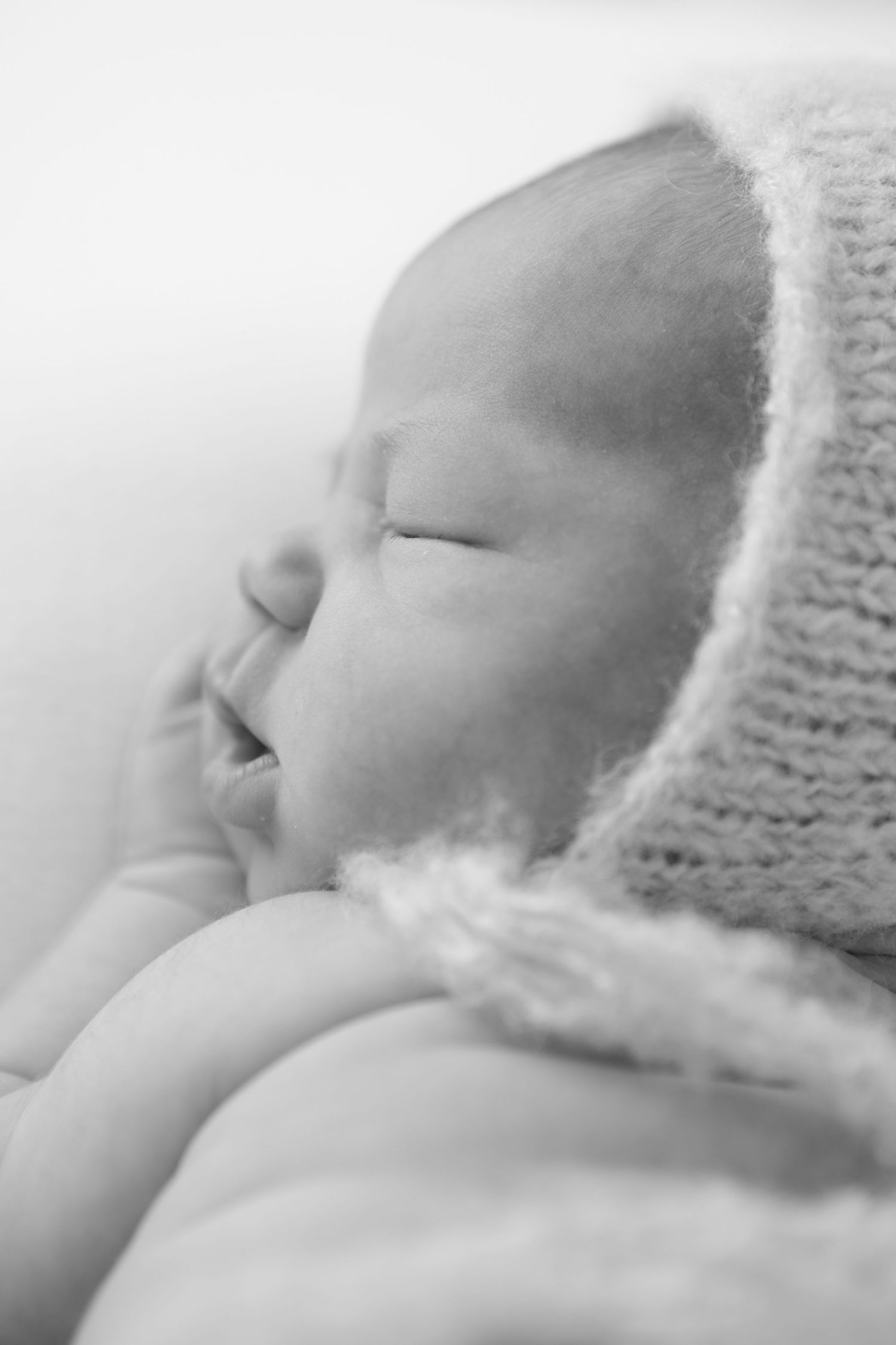 Close-up profile of sleeping newborn wearing soft knitted bonnet in dreamy black and white.