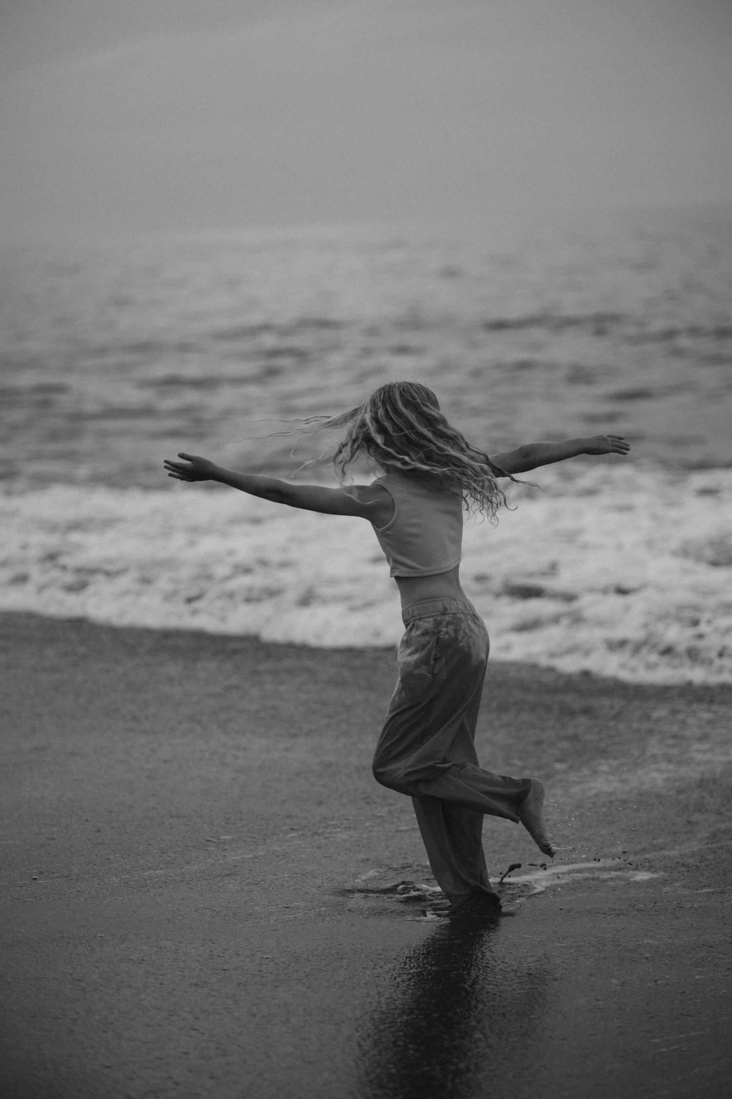 Silhouette of person dancing freely on beach at sunset in black and white.