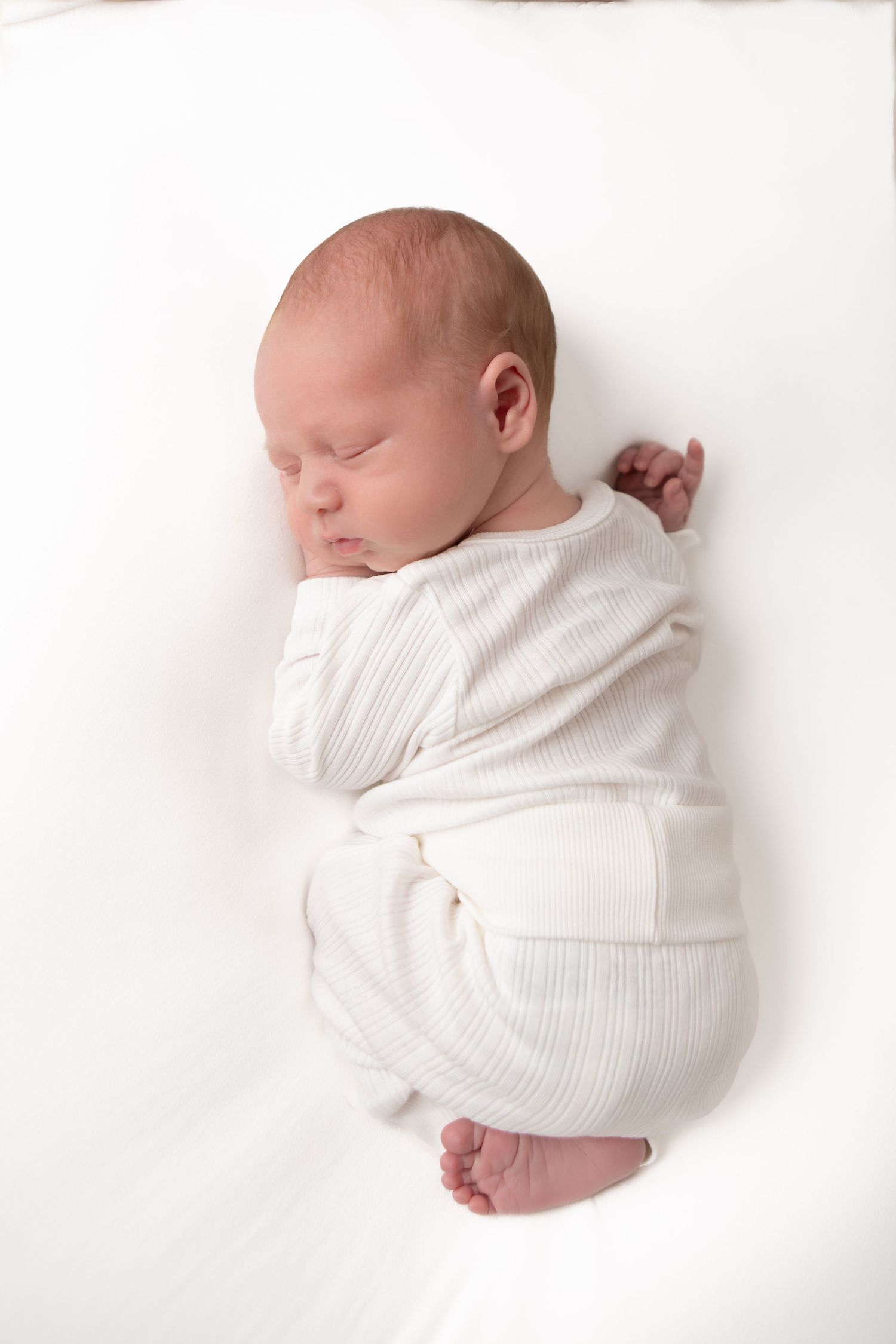 Peaceful newborn baby sleeping swaddled in white knit wrap on soft white background.