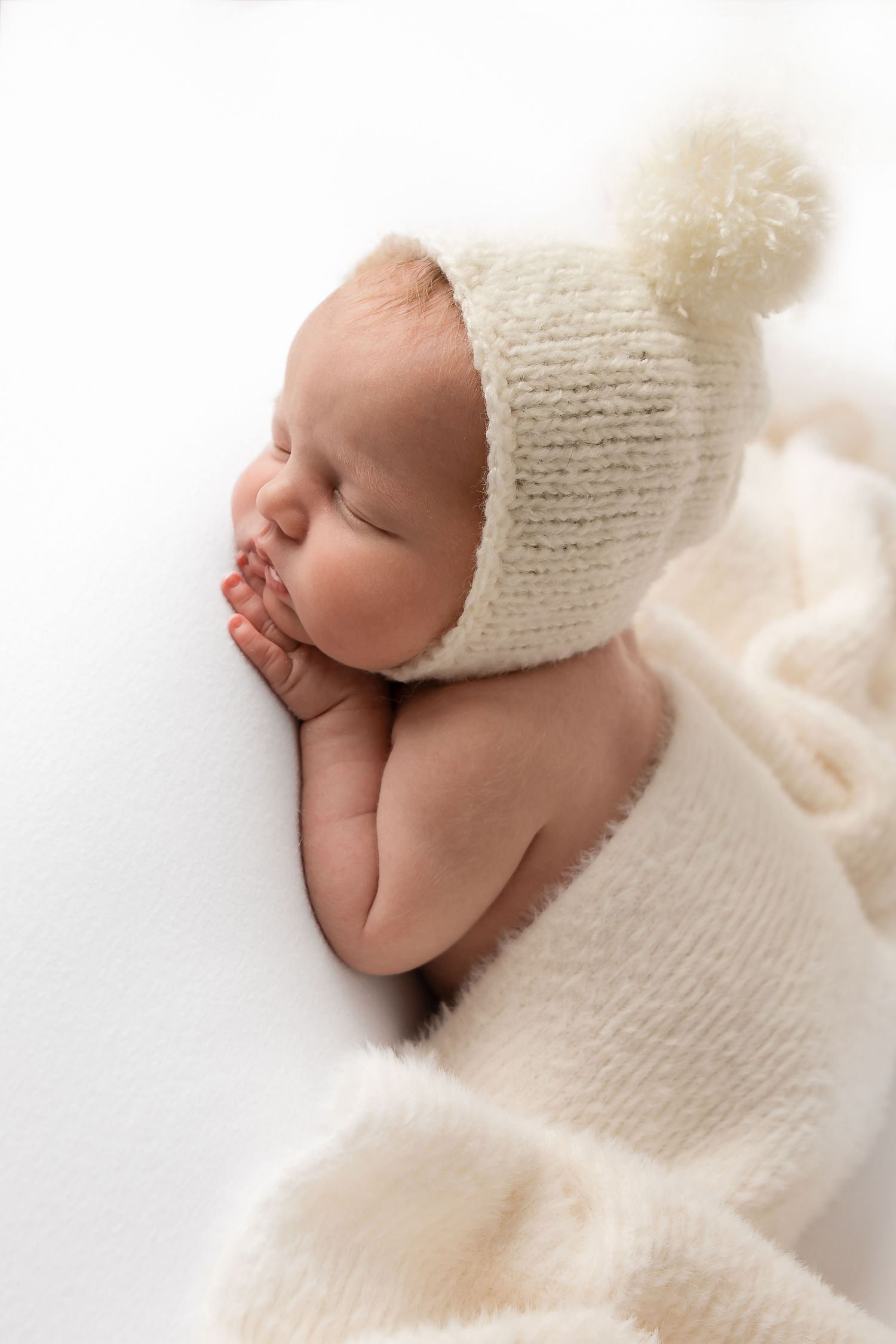 Sleeping newborn baby wearing white knit hat and wrapped in soft blanket.