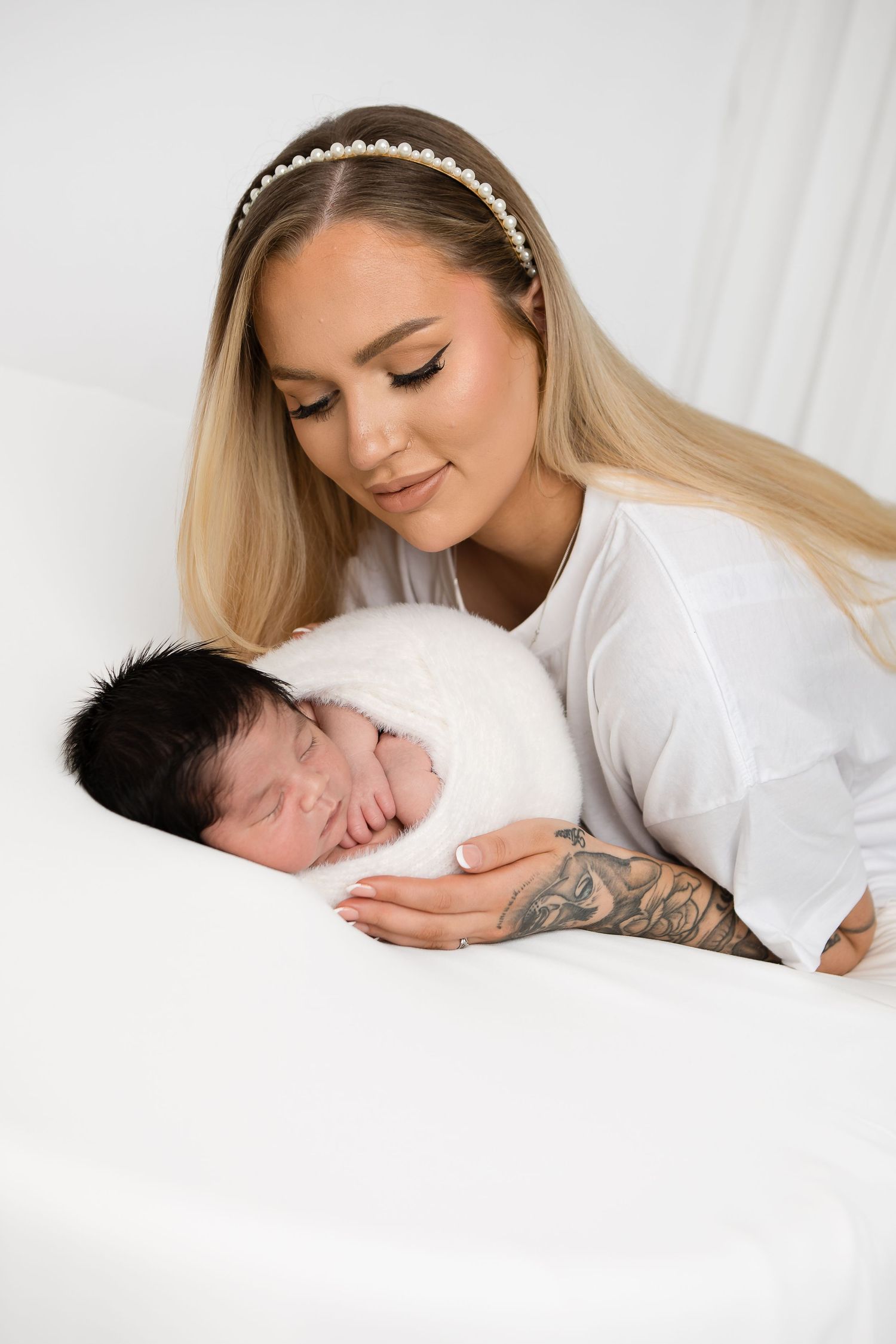 Woman in white gently cradling newborn baby on soft white bedding.