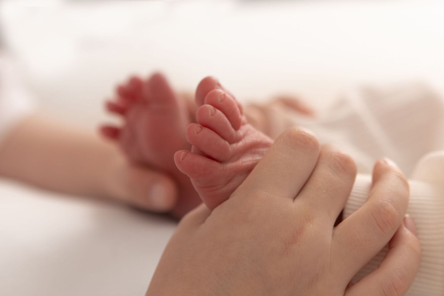 Close-up of a parent gently holding a newborn baby's tiny feet in their hands.