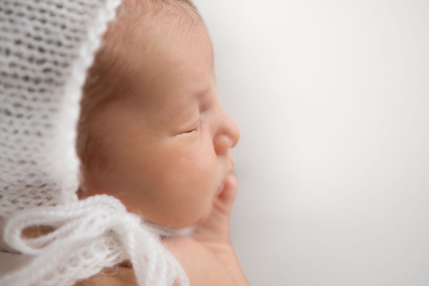 Newborn baby sleeping peacefully wrapped in delicate white knit fabric.