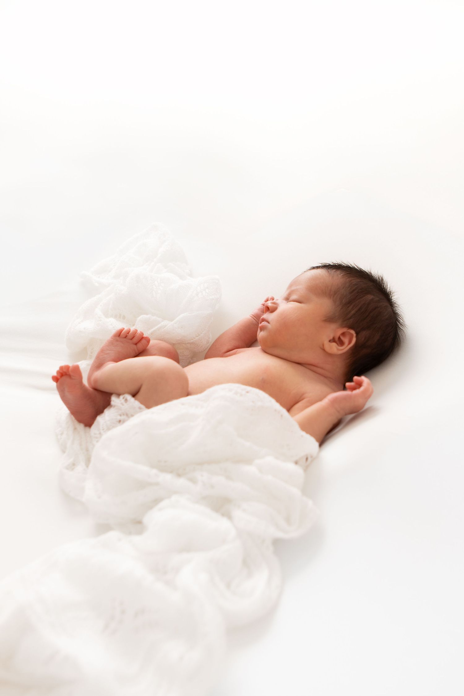 A peaceful newborn baby sleeping wrapped in a soft white blanket on a white background.