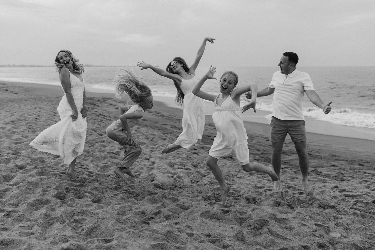 Family having fun and running together on sandy beach in black and white.