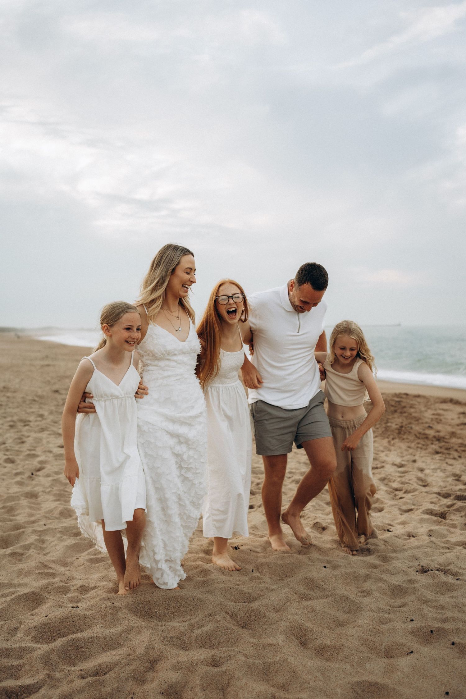 A family shares laughter while walking together on a sandy beach.