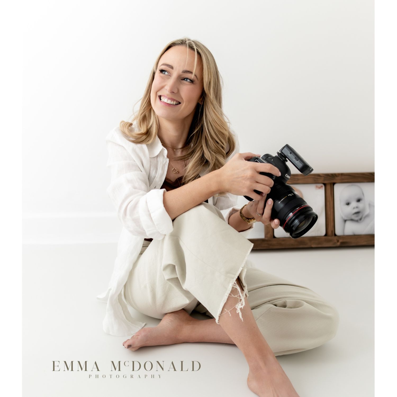 Professional photographer in white sweater lying on floor with camera in casual studio setting.