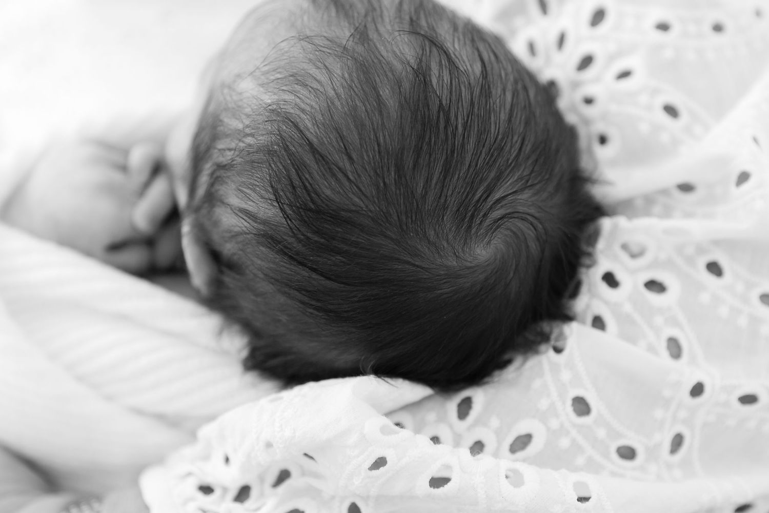 Artistic black and white detail of sleeping newborn on textured white fabric.