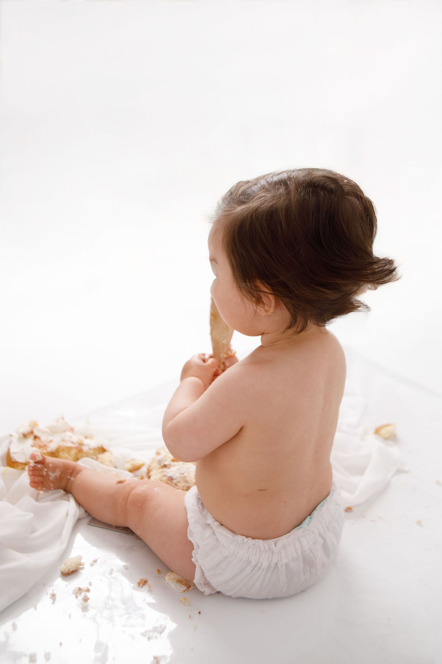 Artistic studio portraits of an infant in white against light background.