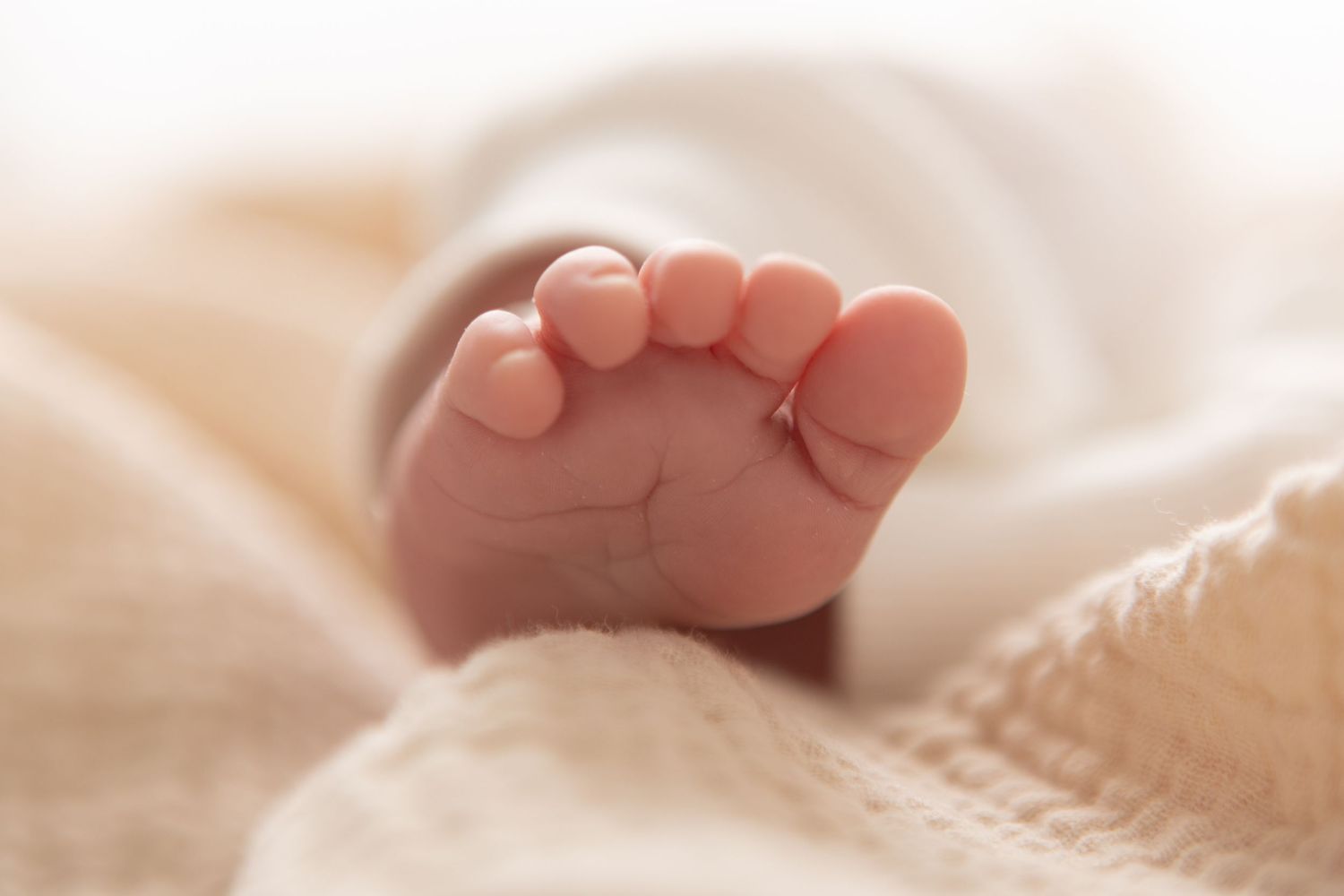 Close-up of a newborn baby's tiny pink foot resting on a soft cream blanket.