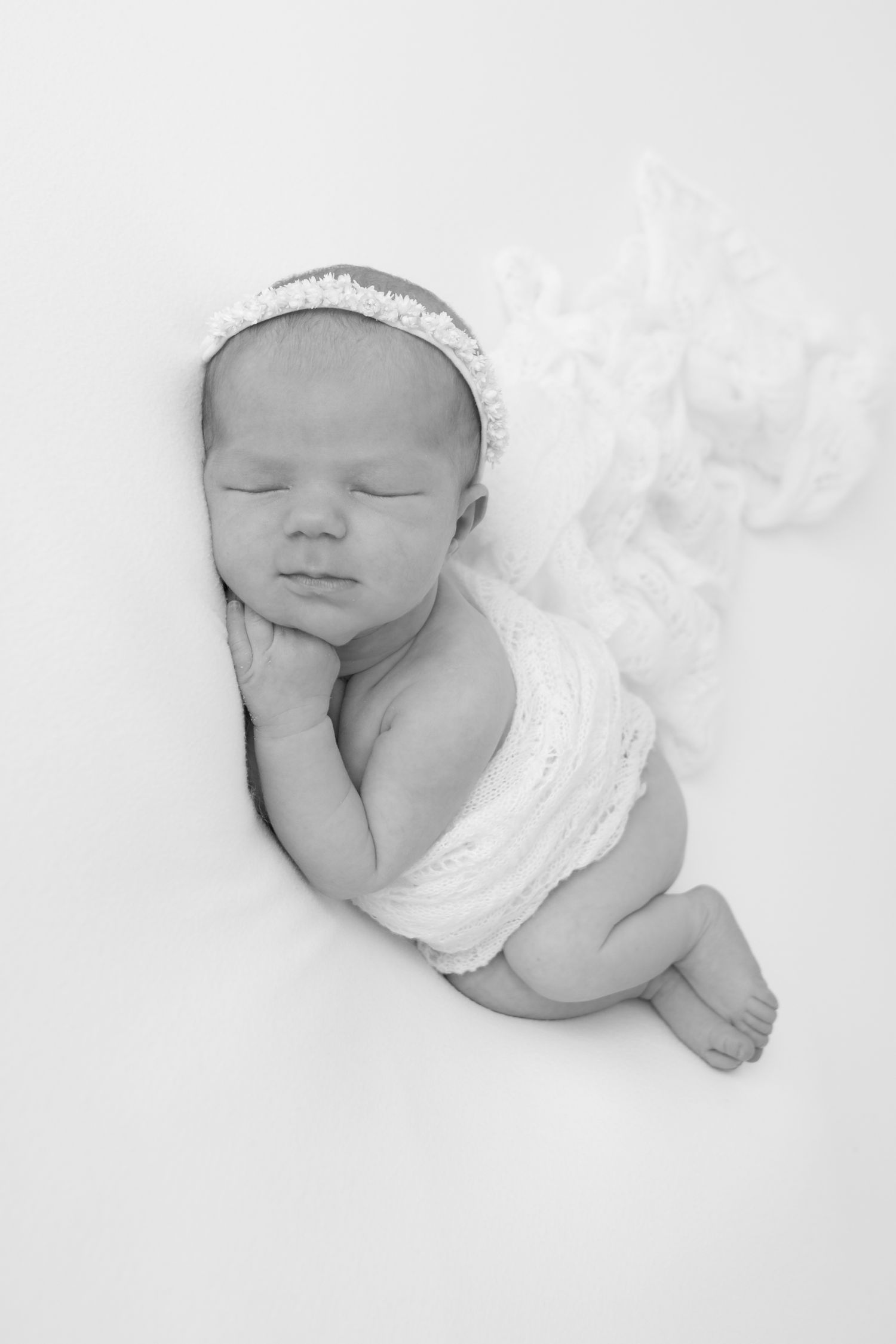 Peaceful sleeping newborn wearing a delicate lace wrap and headband on white background.