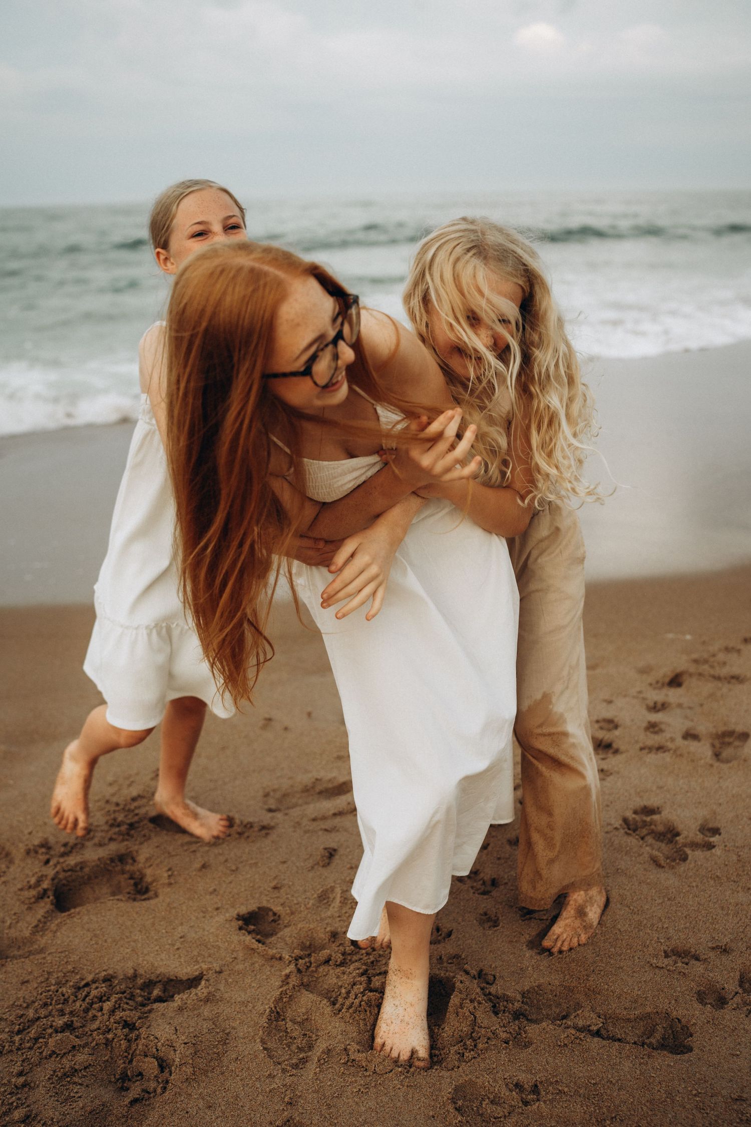 Three people share joyful moments playing together on a beach with waves in the background.