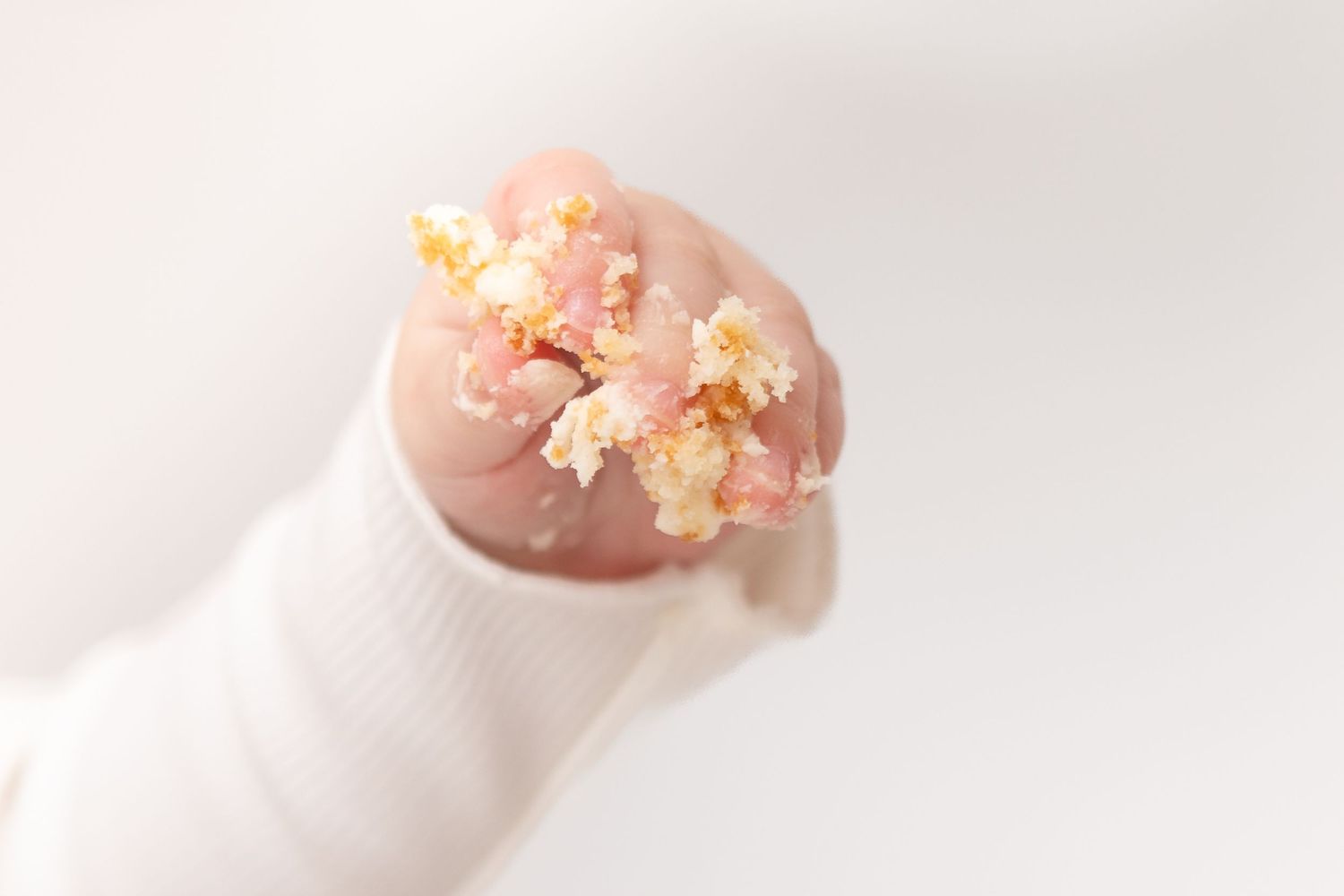 A baby's tiny hand clutching delicate dried flowers with golden accents, wearing a white sleeve.