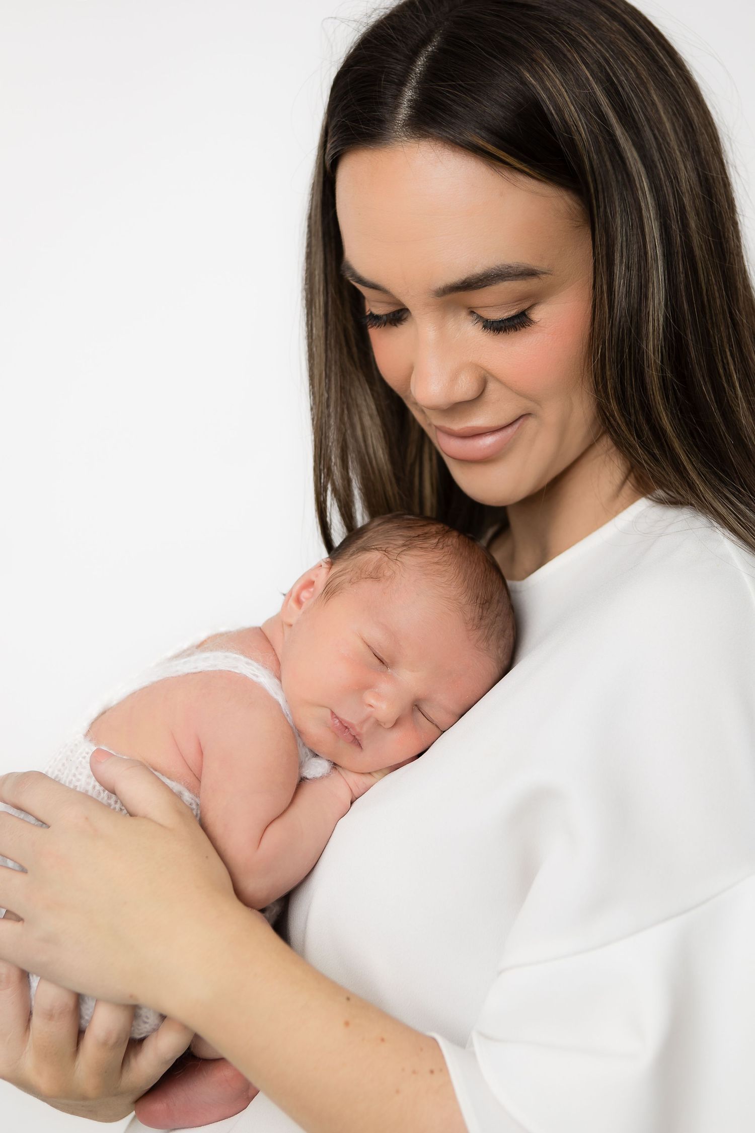 Mother in white holding sleeping newborn baby in intimate portrait series.