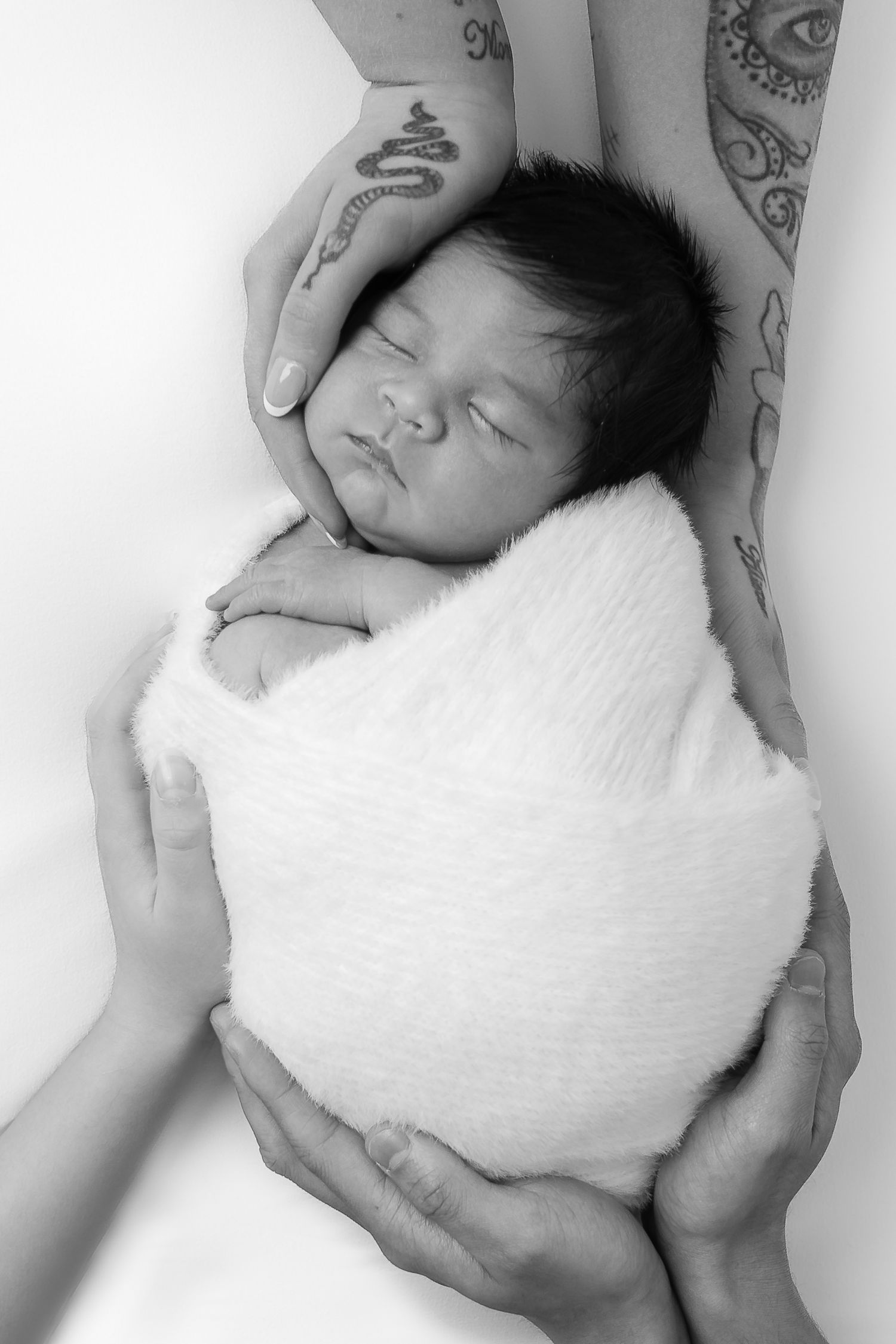 Black and white portrait of newborn baby wrapped in white blanket.