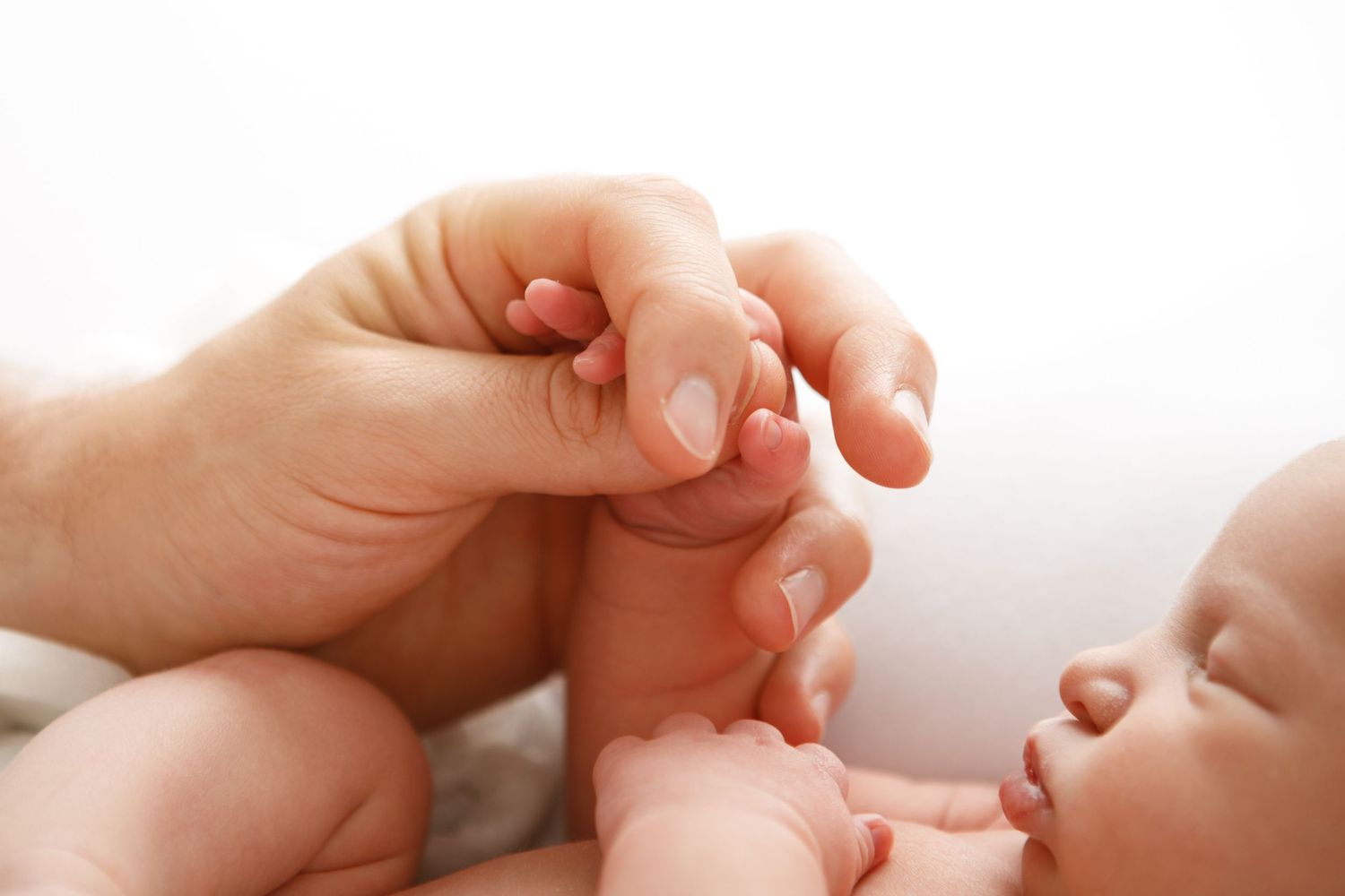 Gentle close-up of parent and baby hands touching.